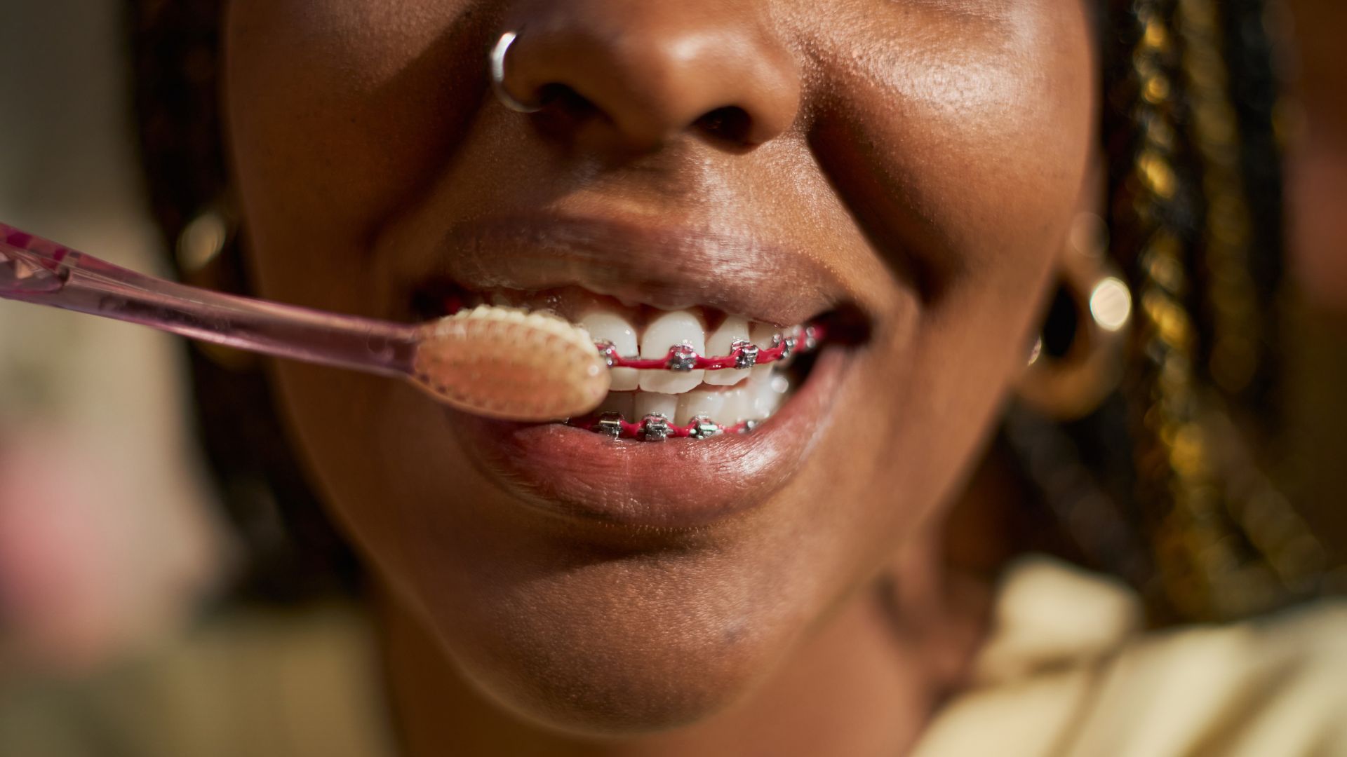 Teen smiling with metal braces and pink bands while brushing teeth with a soft toothbrush