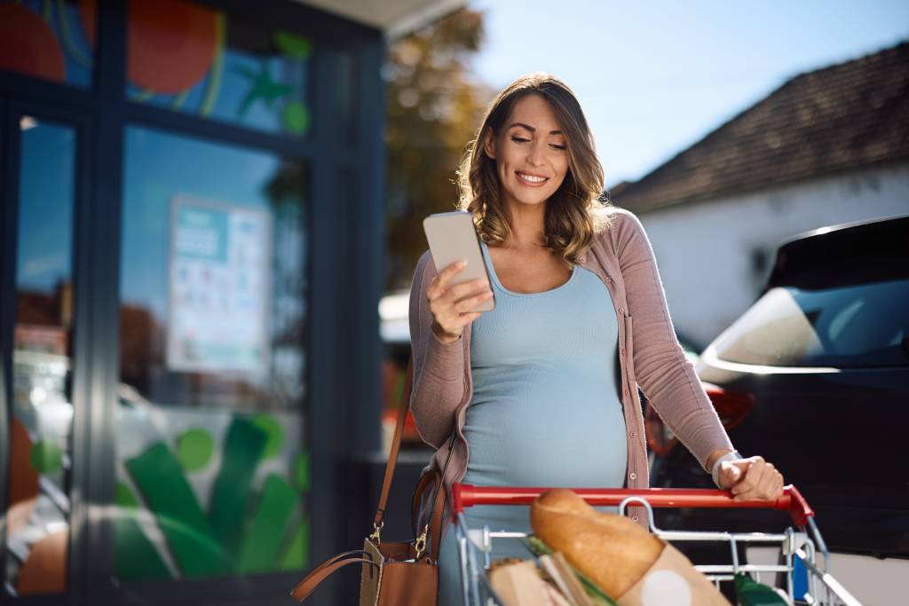 pregnant woman using app on cell phone in front of the supermarket
