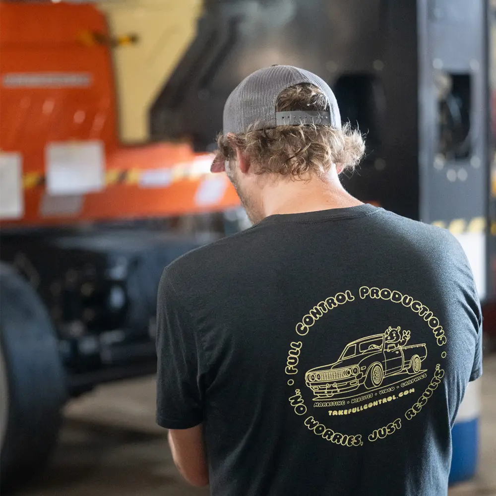 Person wearing a black t-shirt and gray mesh cap facing away, with a graphic of a car and text on the shirt's back.
