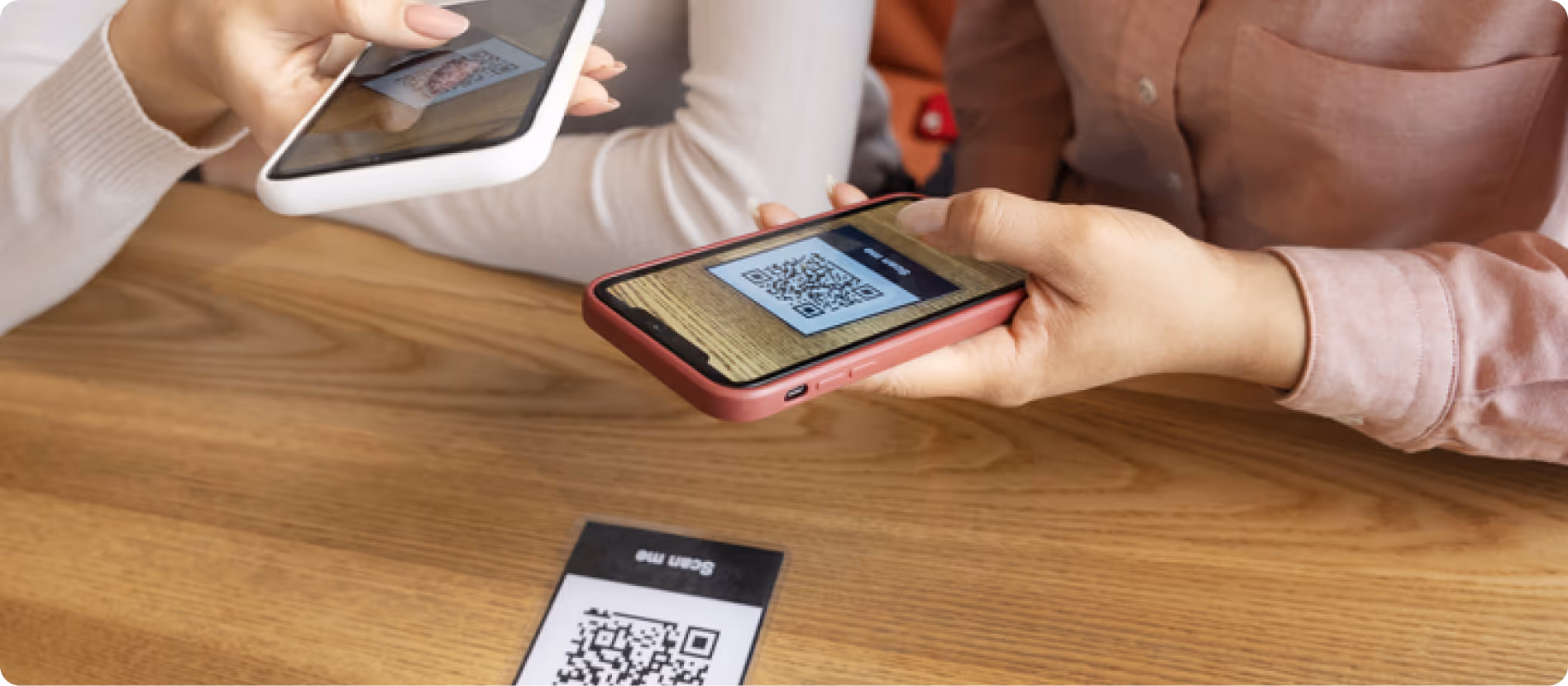 Two people exchanging digital information by scanning QR codes on their smartphones over a wooden table.