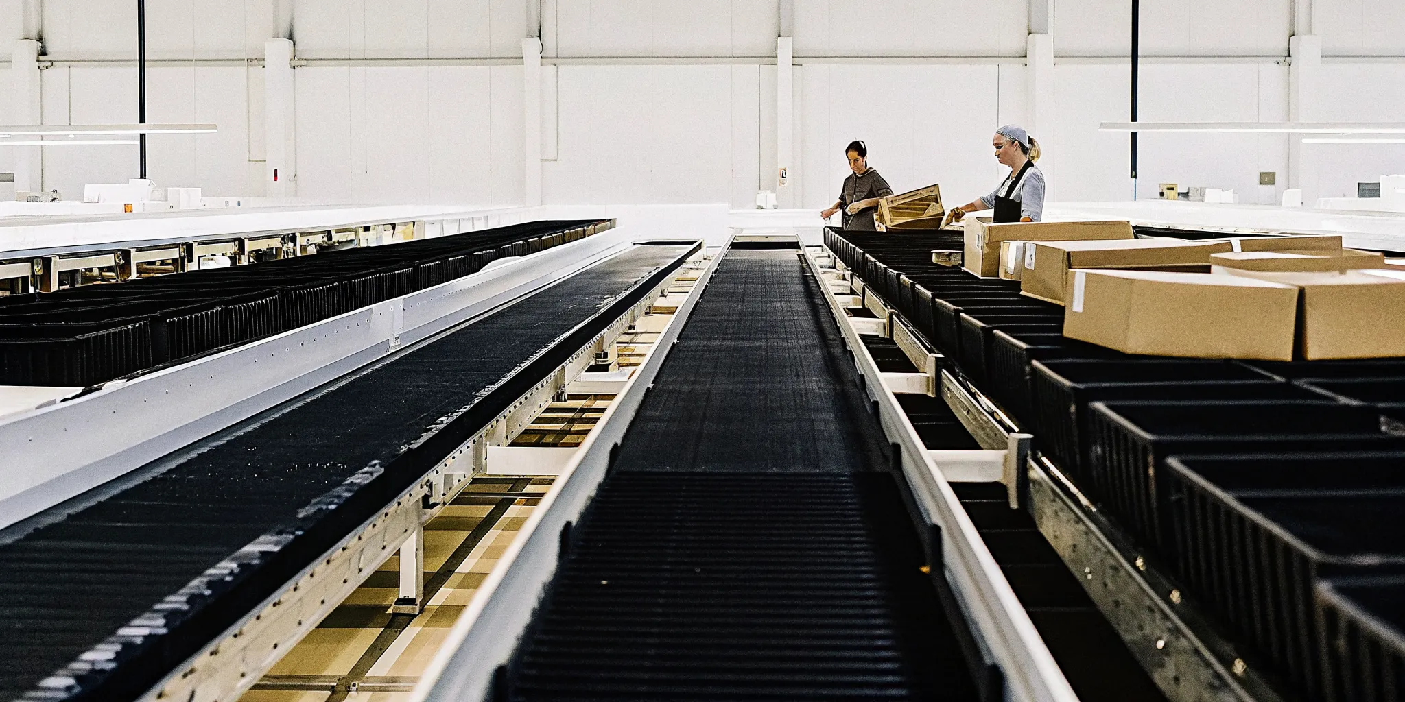 Industrial returns processing facility with conveyor systems and workers at inspection stations sorting products under bright warehouse lighting