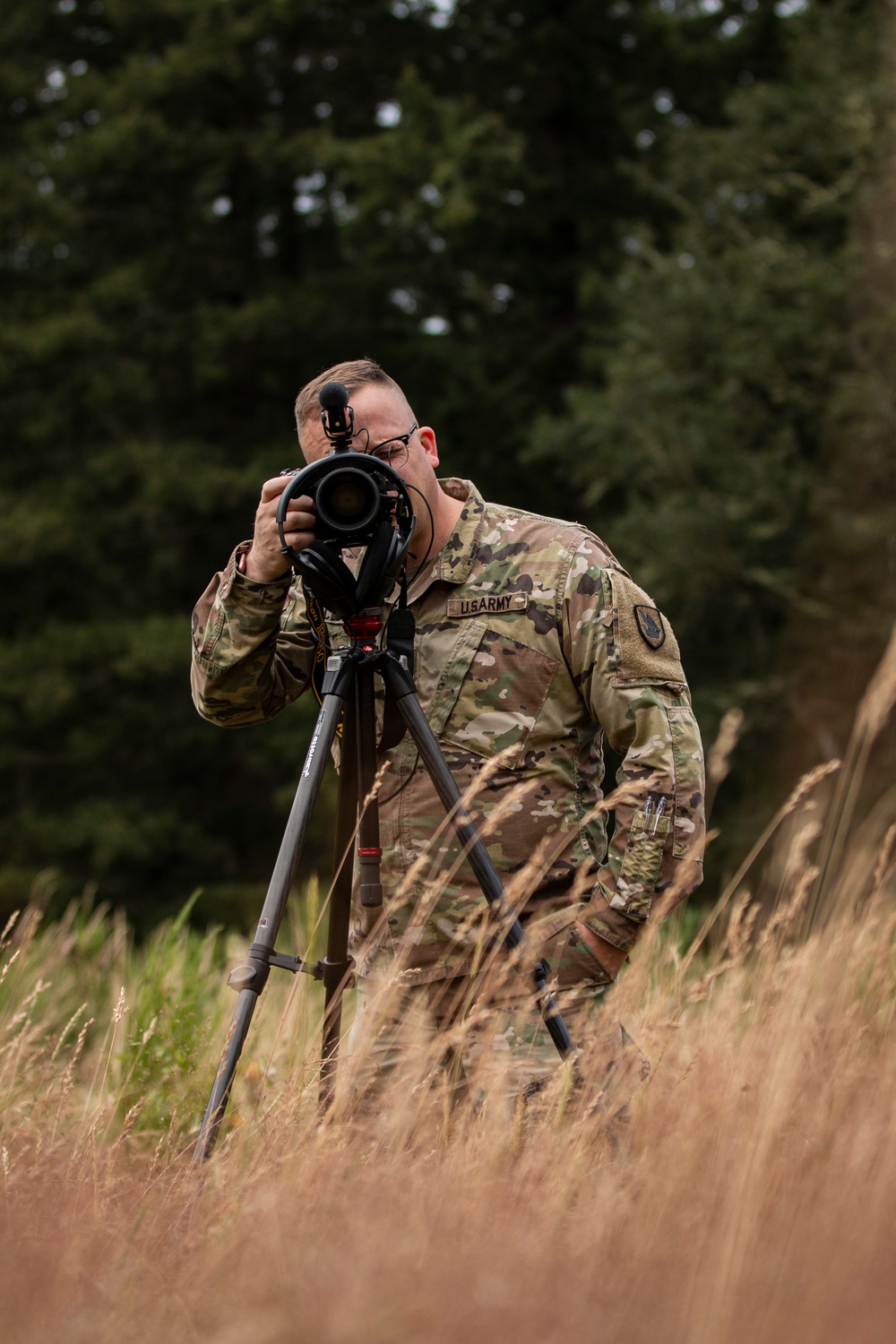 A soldier sets up a camera on a tripod in the field