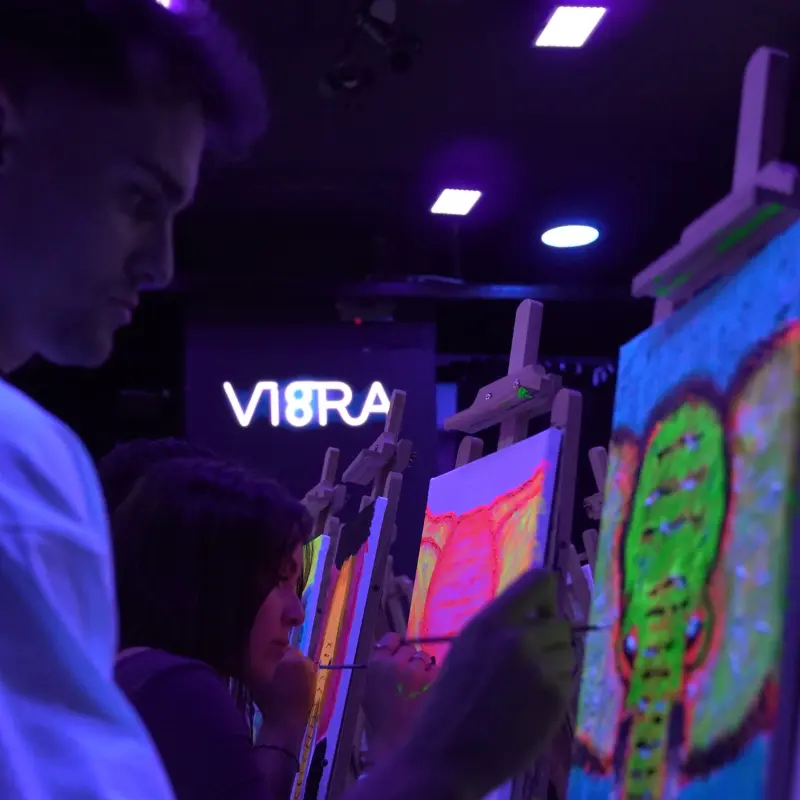 Joven pintando bajo luz neón con el logo de VI8RA al fondo