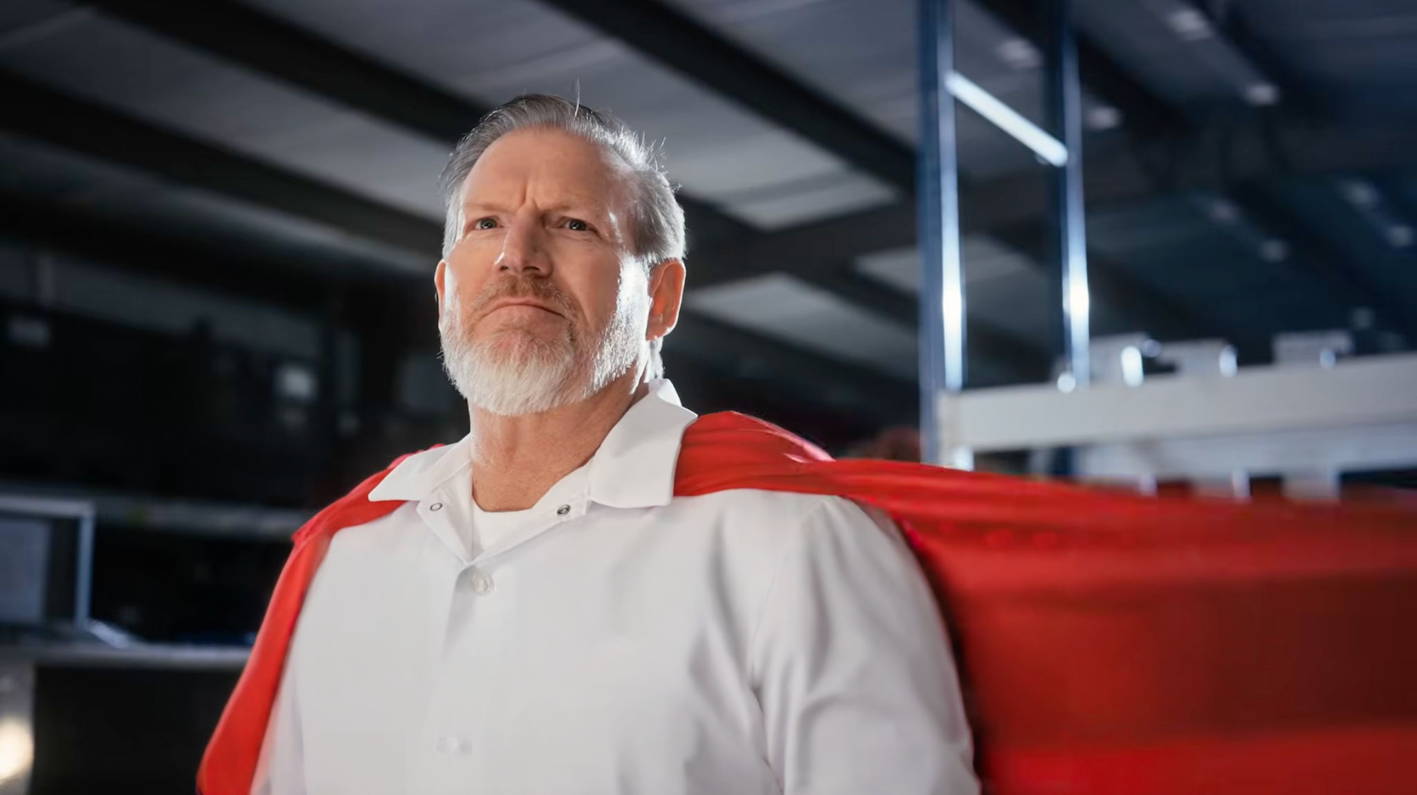 Man wearing a white polo and red cape in a workshop