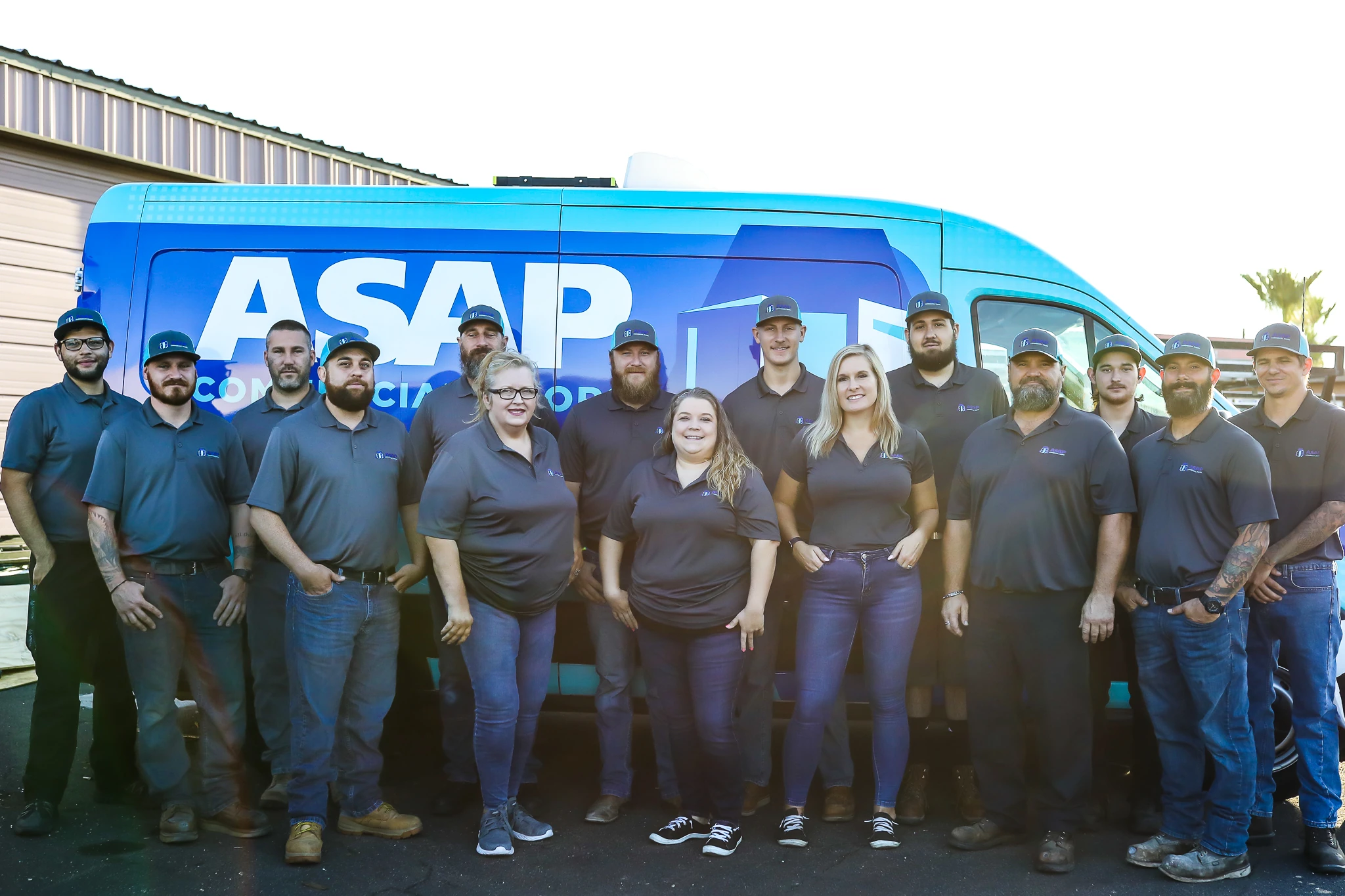 The ASAP Commercial Doors team in branded uniforms standing in front of their wrapped service van.
