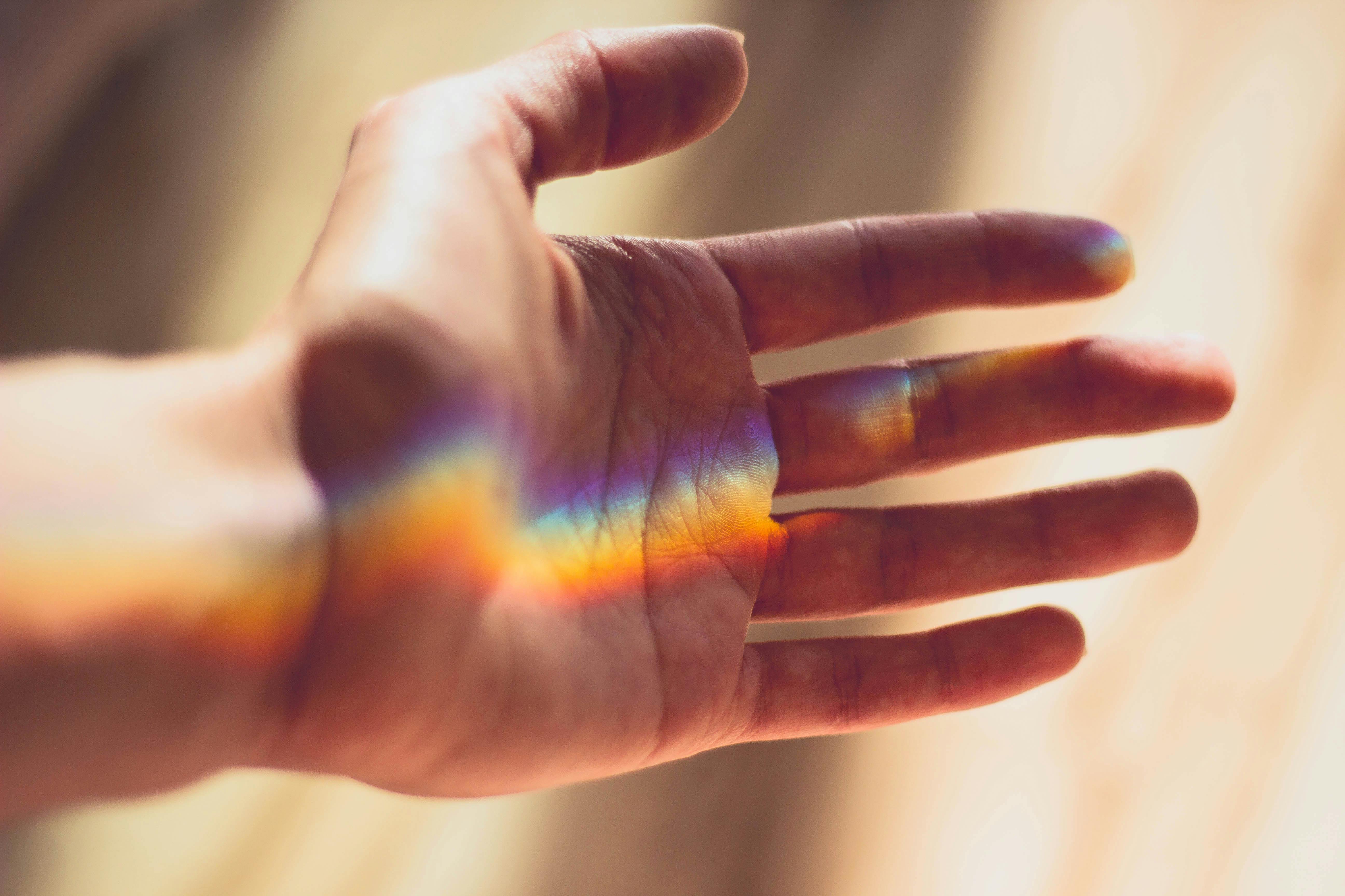 Soft rainbow light falling on a hand during quiet reflection, representing mindfulness and gentle self-connection.