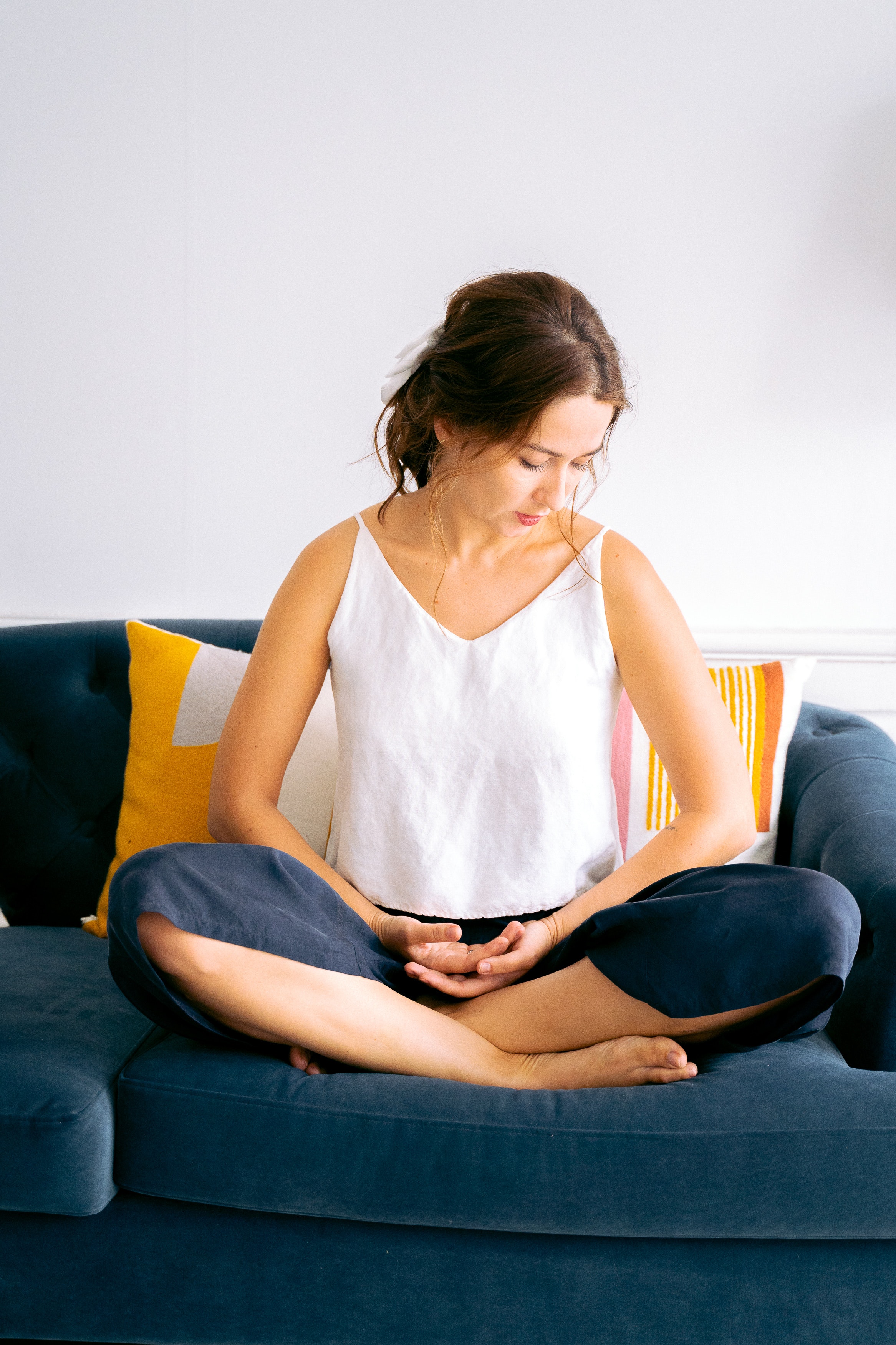 Woman sitting quietly on a blue couch, hands softly in her lap, gaze turned inward