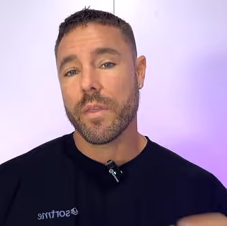 Carl Thompson CEO of SortMe  wearing a black shirt and a small microphone clipped on it, against a light purple background.