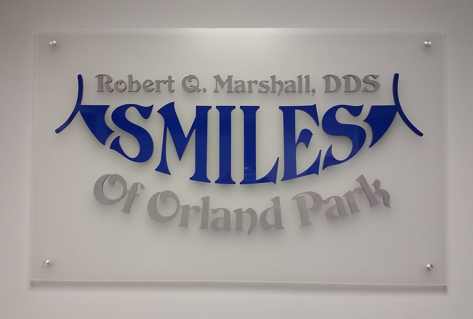 Sign reading 'Robert Q. Marshall, DDS SMILES Of Orland Park' with 'SMILES' in large blue letters and the rest in gray.