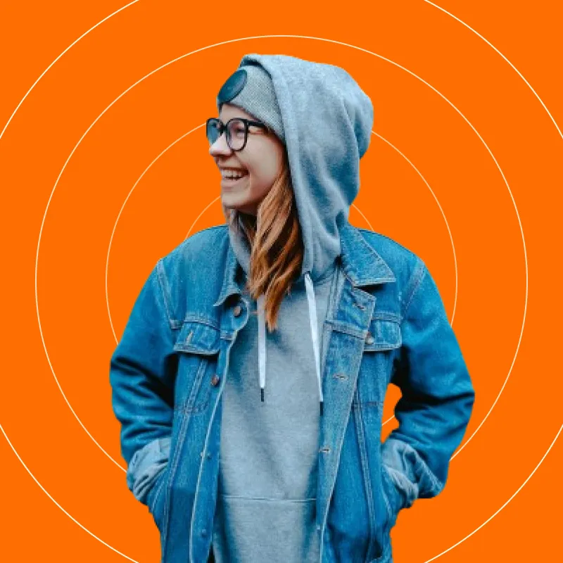 A woman wearing a hoodie and glasses standing in front of an orange background.