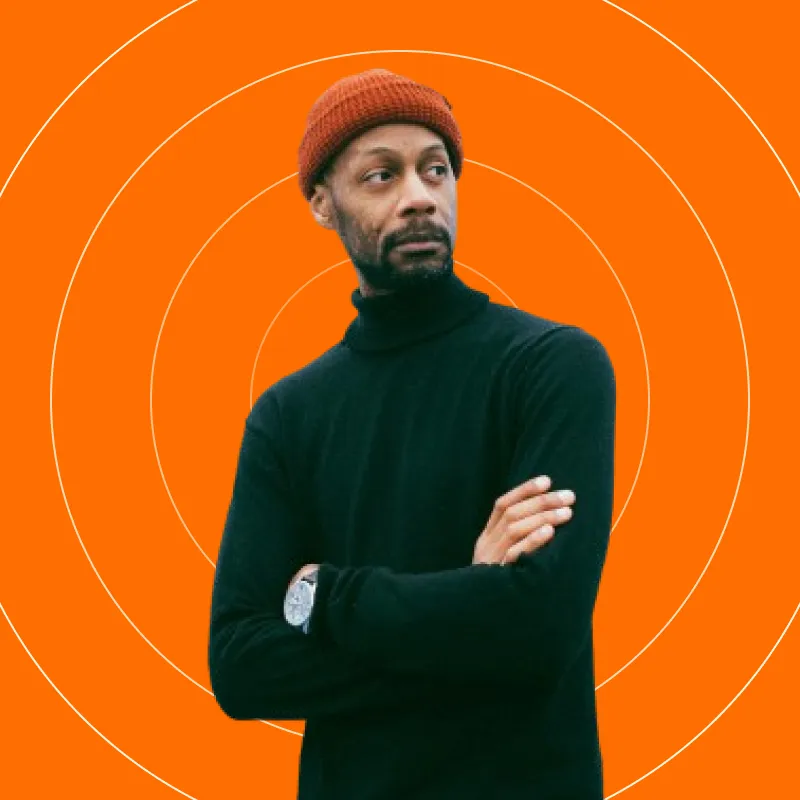 A man with his arms crossed standing in front of an orange background.