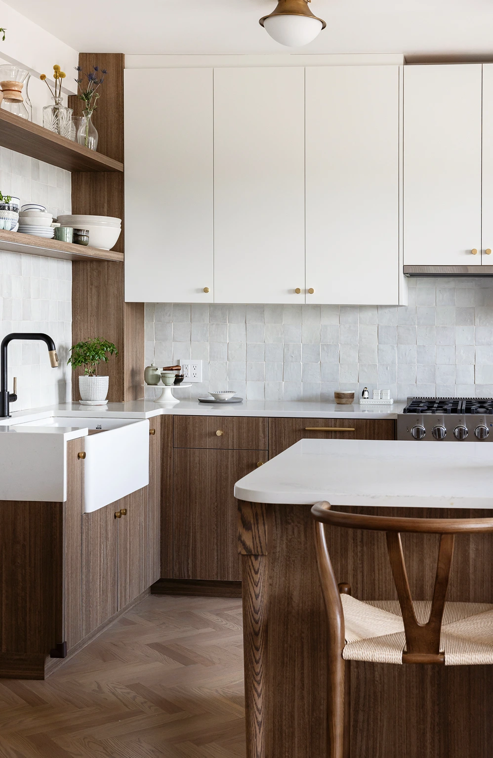 Modern kitchen with white upper cabinets, wood lower cabinets, marble countertops, and a wooden chair.