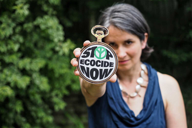 Image of a woman holding a badge that says "Stop Ecocide Now" 