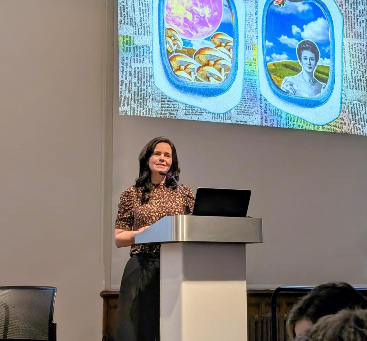 A woman stood at a podium in front of a screen.