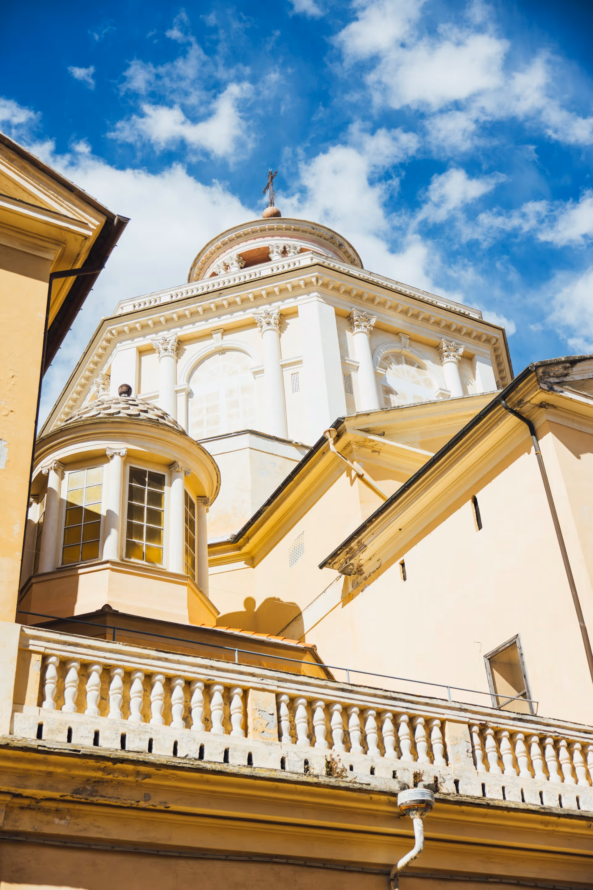 Blick auf die weiße Kuppel einer Kirche mit Säulen und Fenstern vor blauem Himmel mit Wolken.