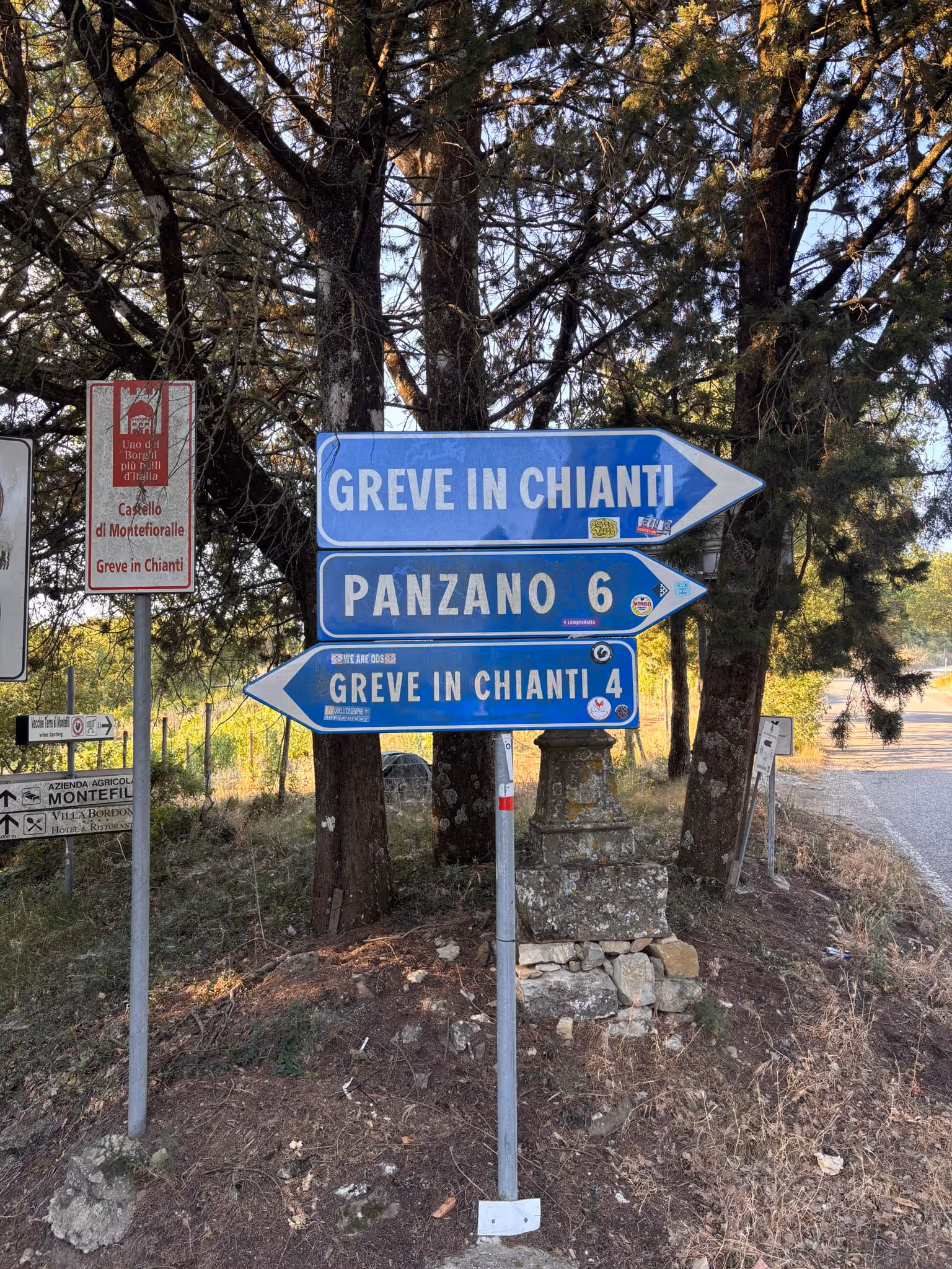 Straßenschilder an einem Baumstamm in einer ländlichen Gegend mit Angaben zu Greve in Chianti und Panzano, Toskana, Italien.