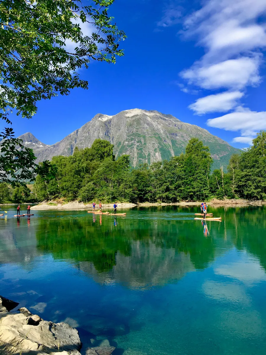 Summer in Norway, a group with paddleboards makes their way downstream a river.