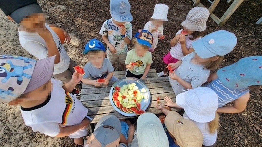 Kinder der elbzwerge Kita Stellingen am Picknicktisch im Schatten mit einer großen Schale Wassermelone und Gurken