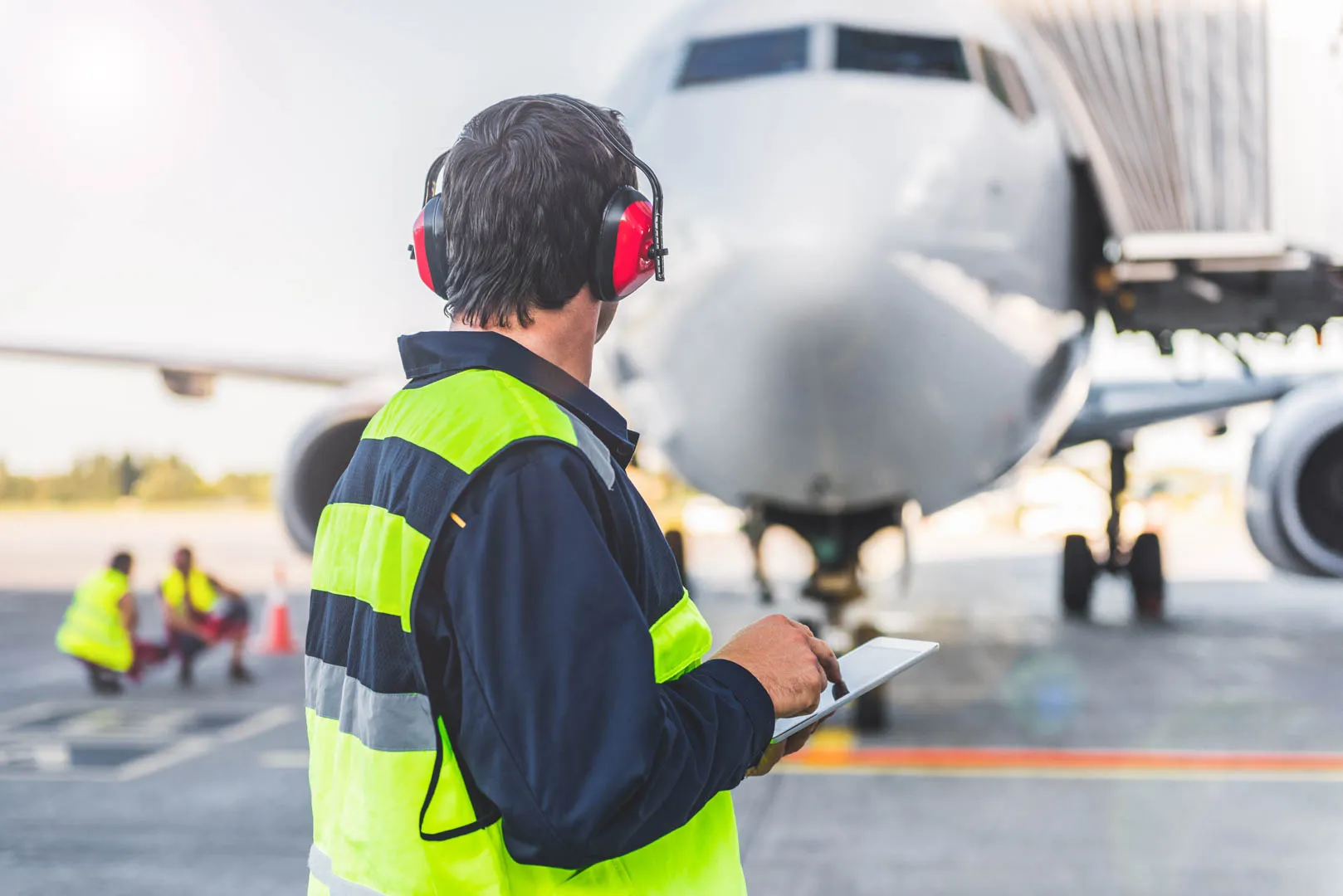 A worker standing on a runway tarmac holding a clipboard with an airplane behind him.
