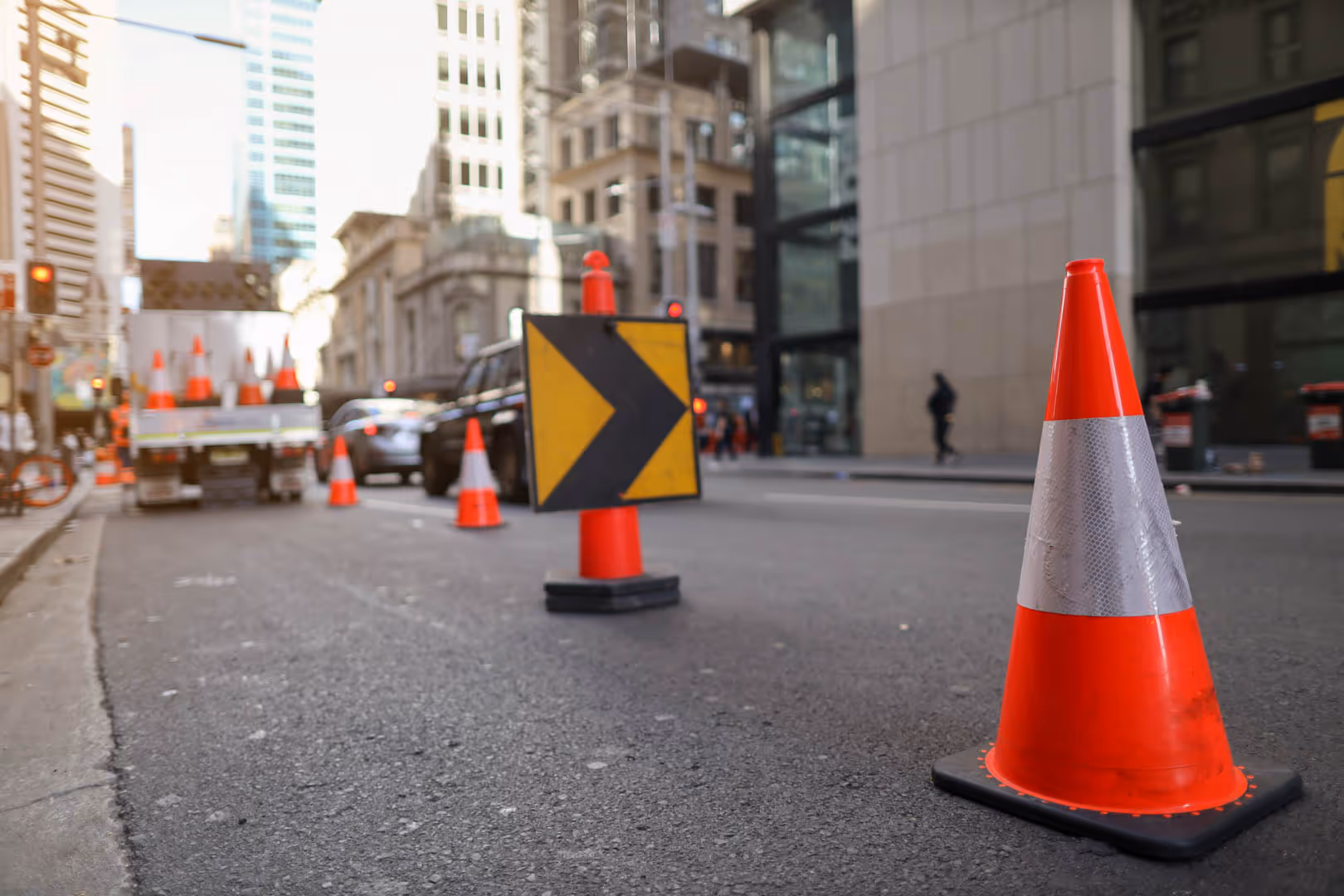 Orange traffic cones lining a road with people doing road work.
