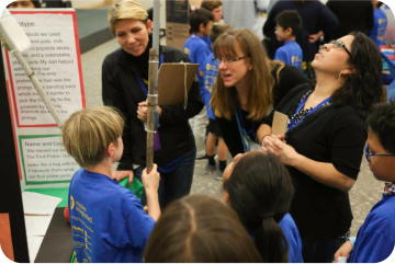 A couple of judges are asking a young boy questions about his invention