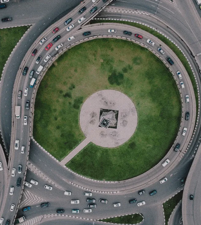 Aerial view of a busy circular roundabout with green grass and a central monument.