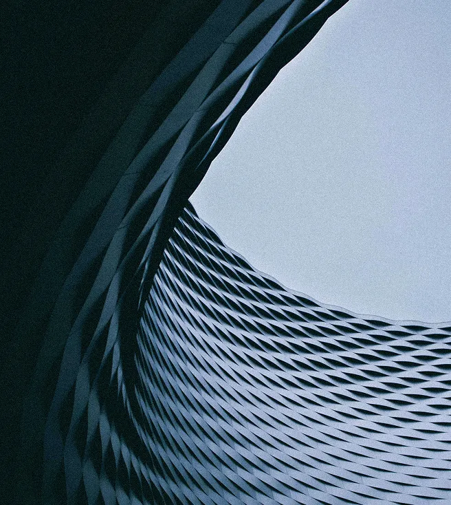 Curved modern architectural structure with a textured, repeating diamond pattern and an open circular sky view above.