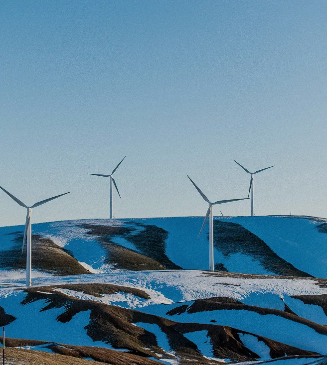 Wind turbines on snowy hills under a clear blue sky during daylight.