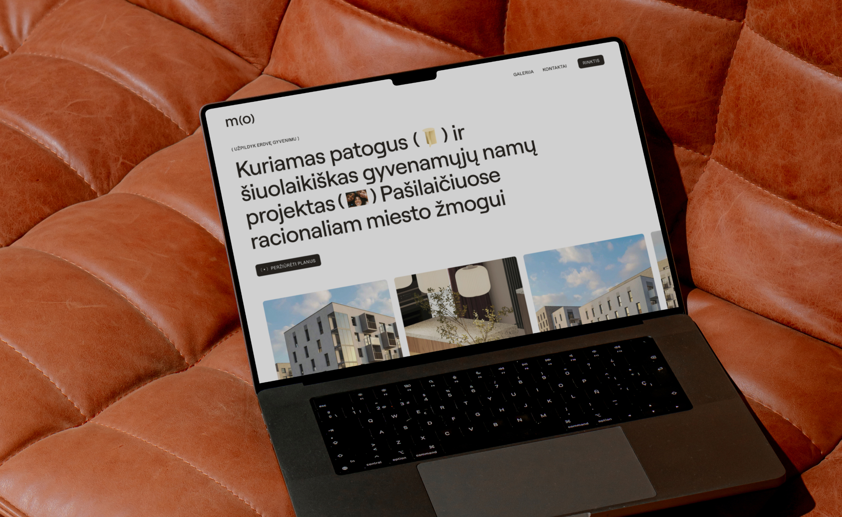 Laptop on brown leather couch displaying a modern housing project website with images of buildings.