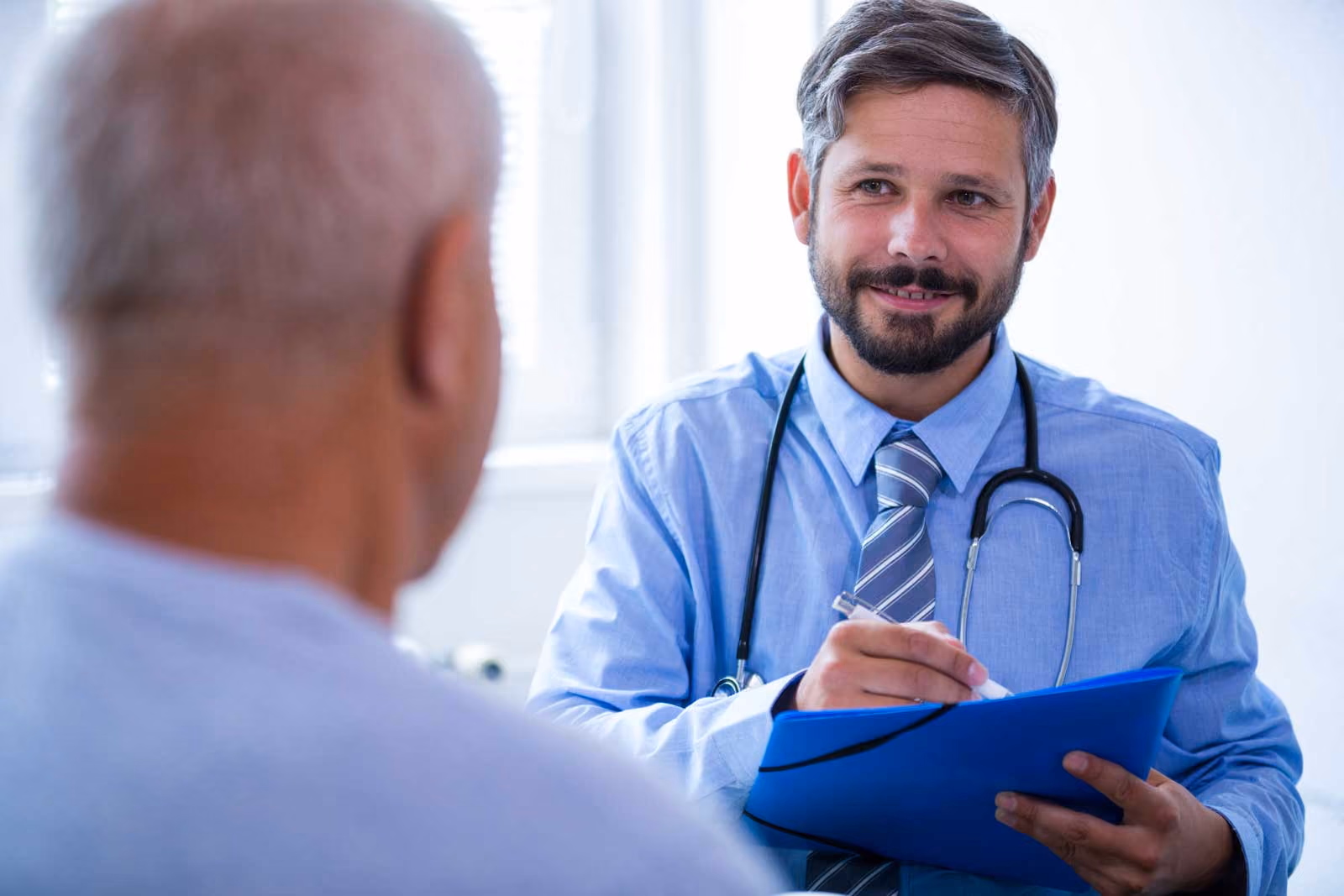 A doctor in a blue shirt and tie talking to a patient.
