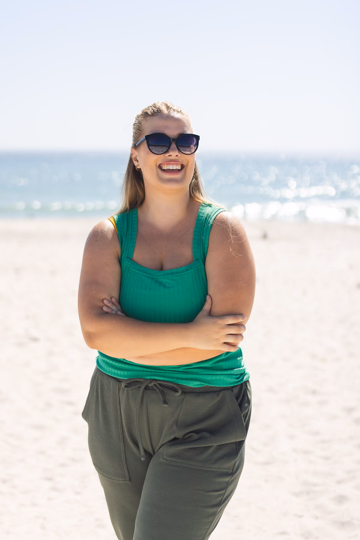 A woman standing on a beach with her arms crossed.