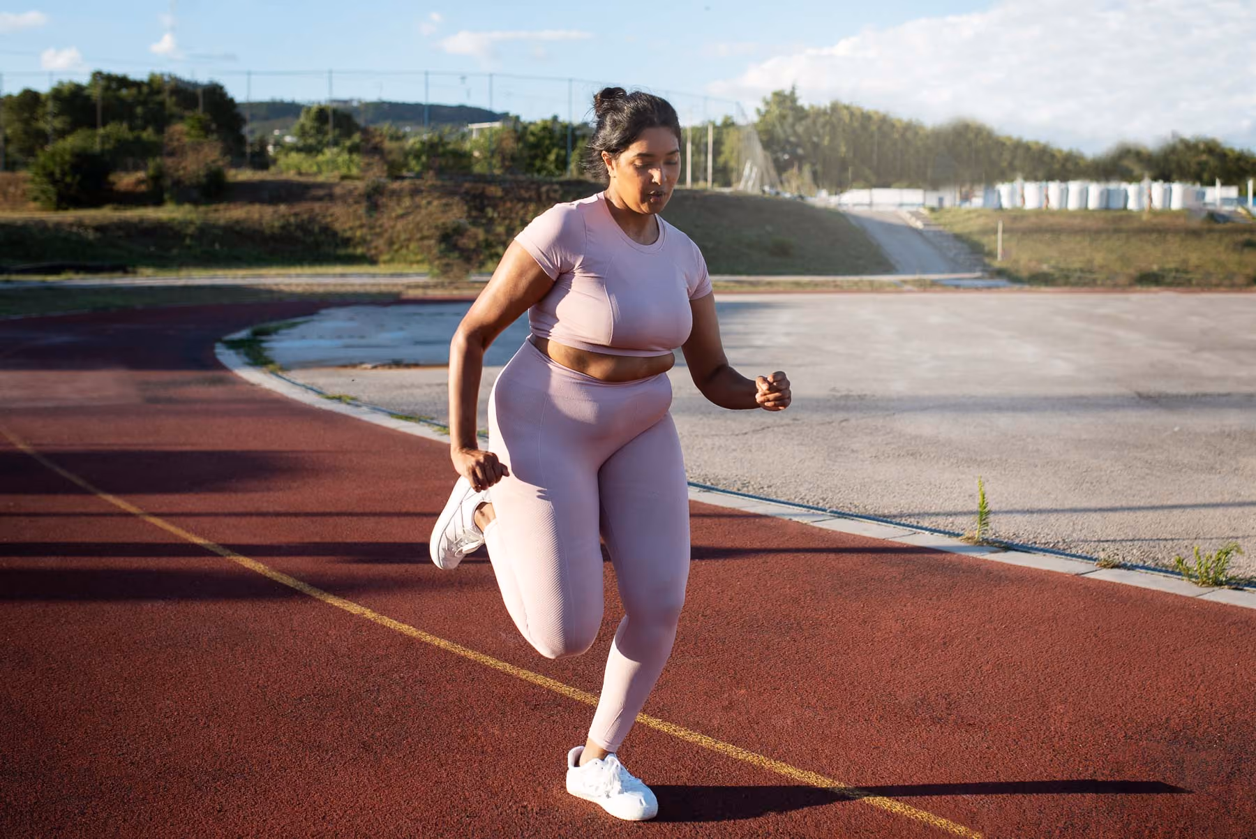 A woman in a pink outfit is running on a track.