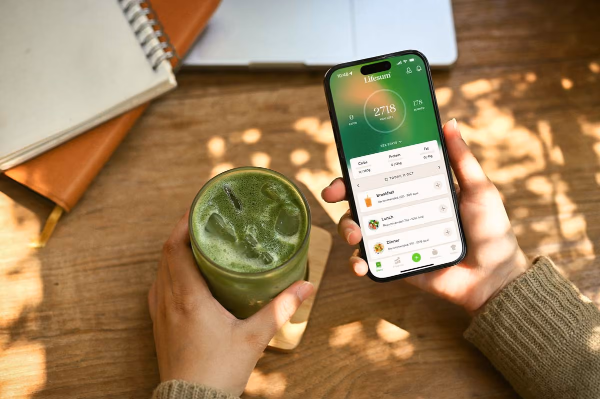 A person holding a cell phone next to a green drink.
