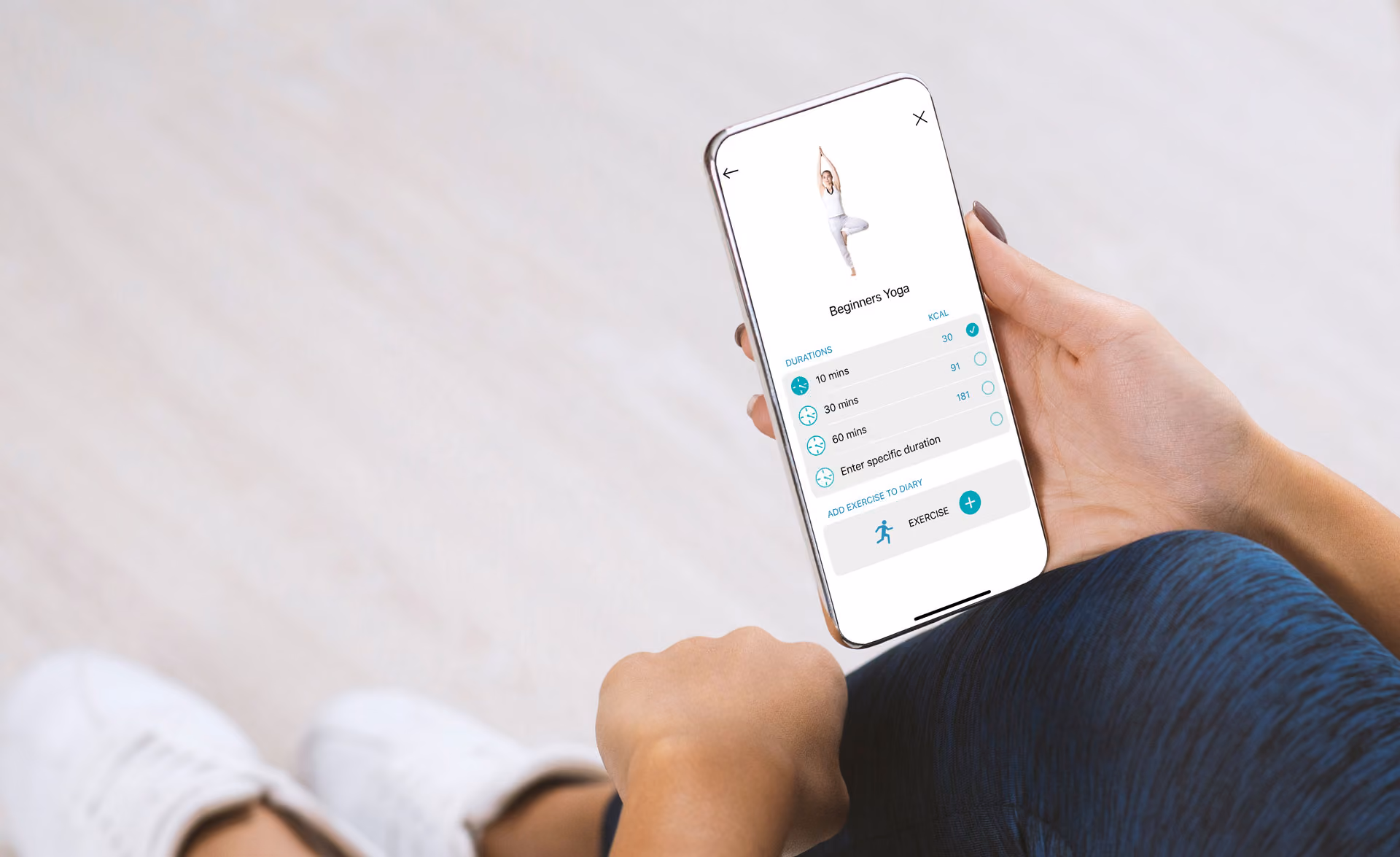 Hand holding smartphone displaying beginner yoga workout app with duration options and exercise tracking.