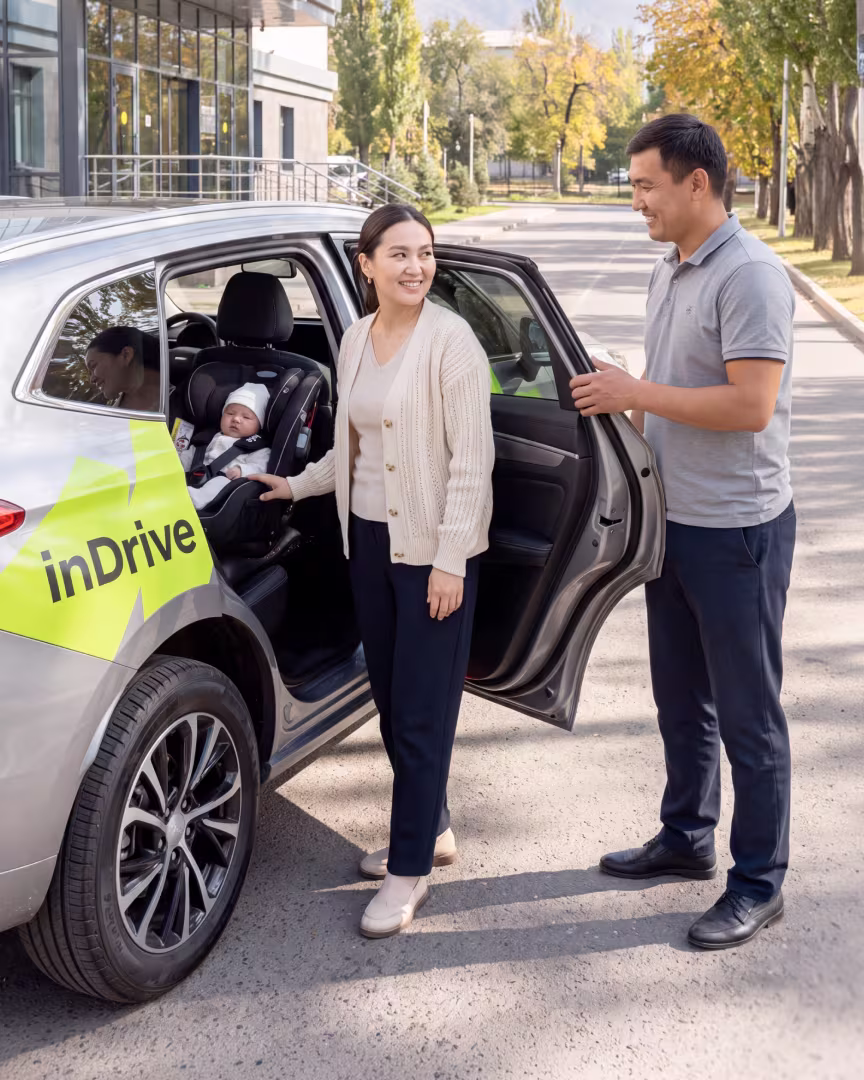 Женщина и водитель inDrive у автомобиля с новорождённым в автокресле
