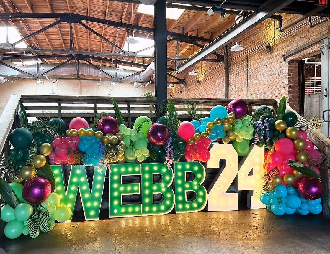 Lit letters spelling HVMS in front of silver and blue balloons at Hardin Valley Middle School with mural stars and music notes on the wall.