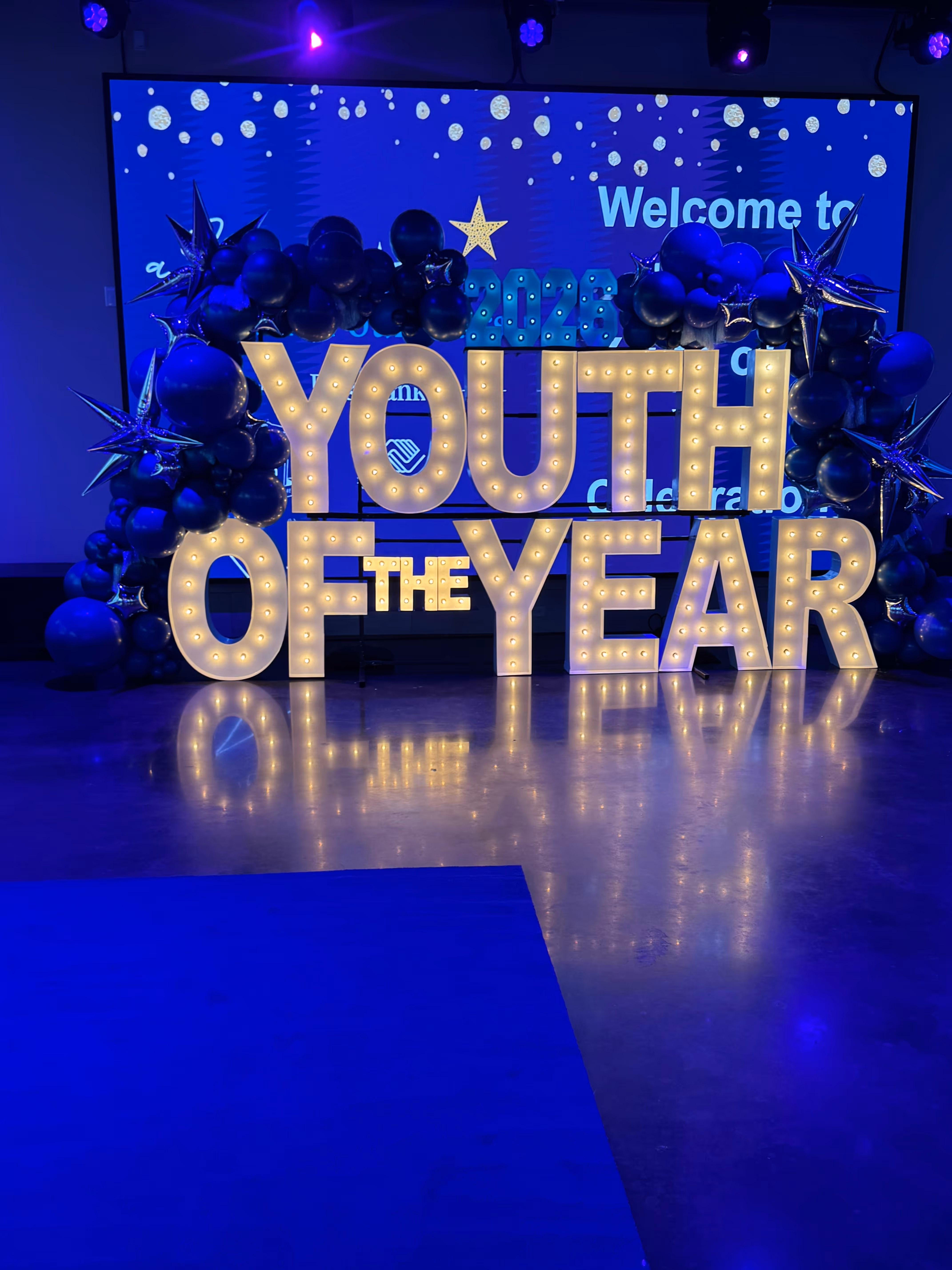Lit letters spelling HVMS in front of silver and blue balloons at Hardin Valley Middle School with mural stars and music notes on the wall.