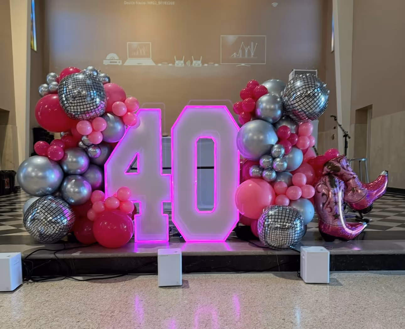 Large illuminated pink number 40 surrounded by pink, silver, and disco ball balloons, with shiny pink cowboy boot balloons on the right.