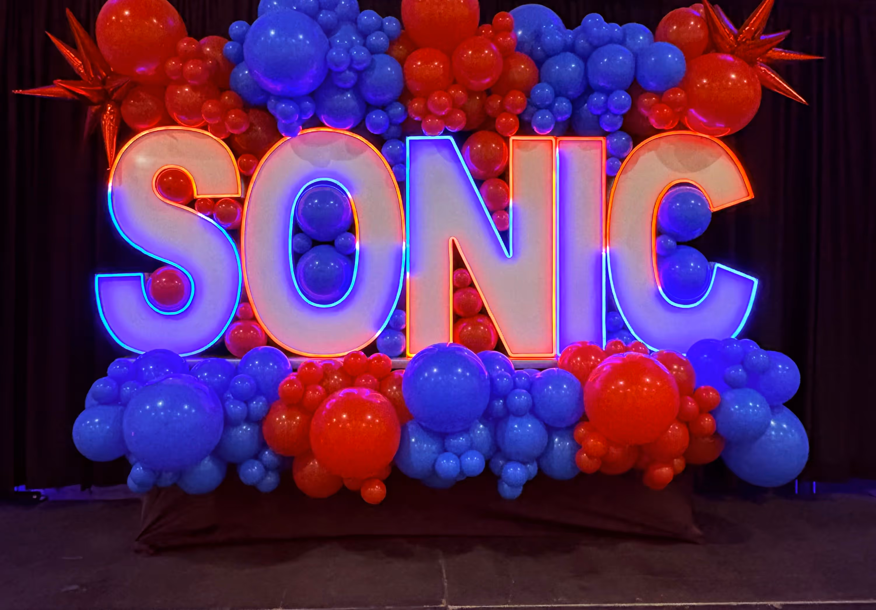 Lit letters spelling HVMS in front of silver and blue balloons at Hardin Valley Middle School with mural stars and music notes on the wall.