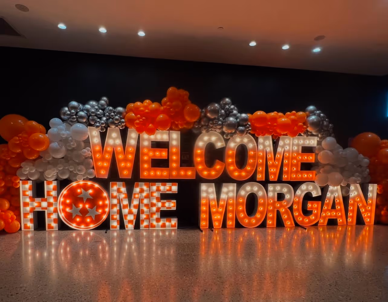 Lit letters spelling HVMS in front of silver and blue balloons at Hardin Valley Middle School with mural stars and music notes on the wall.