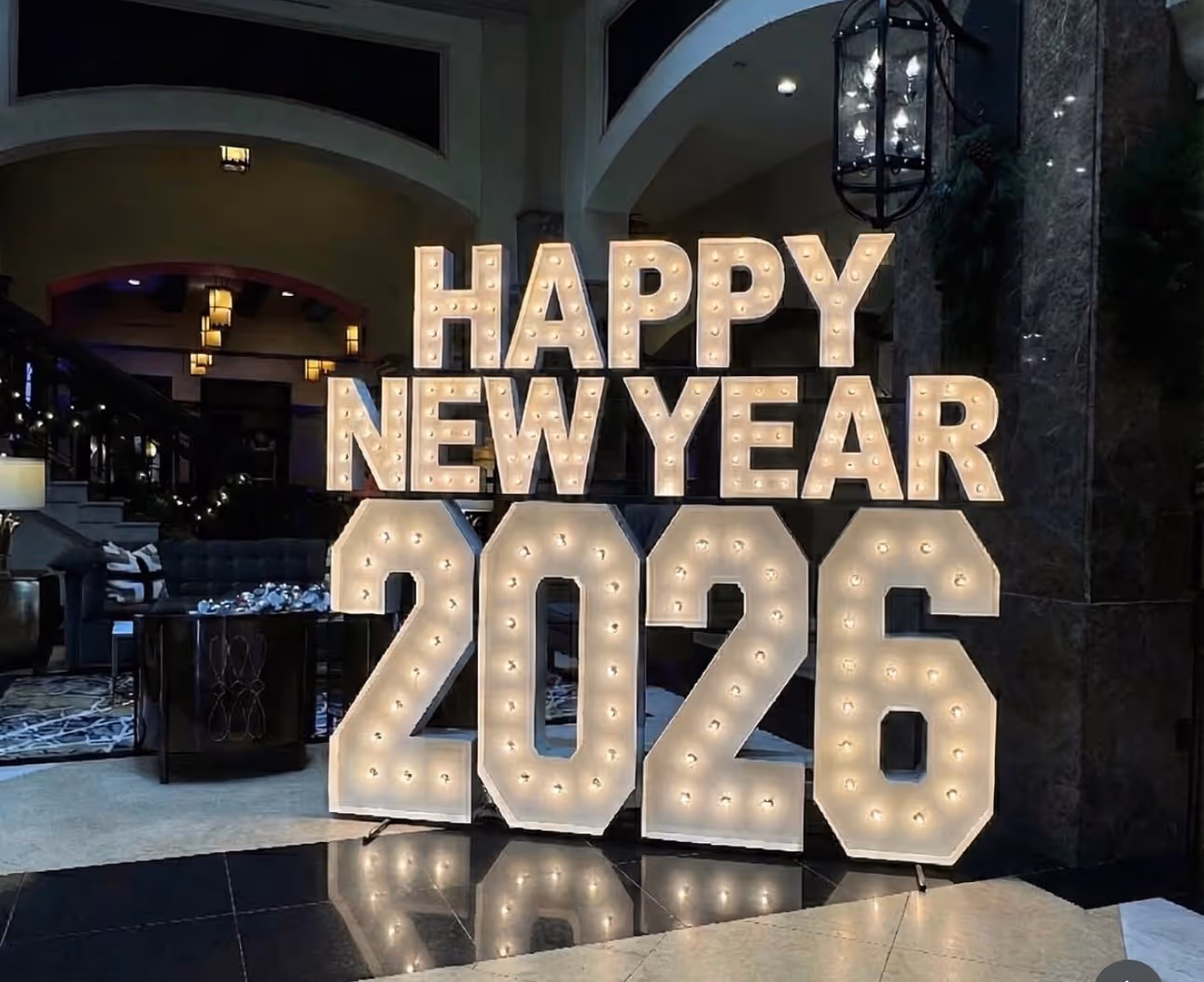 Large illuminated sign displaying 'HAPPY NEW YEAR 2026' inside a warmly lit lobby area.