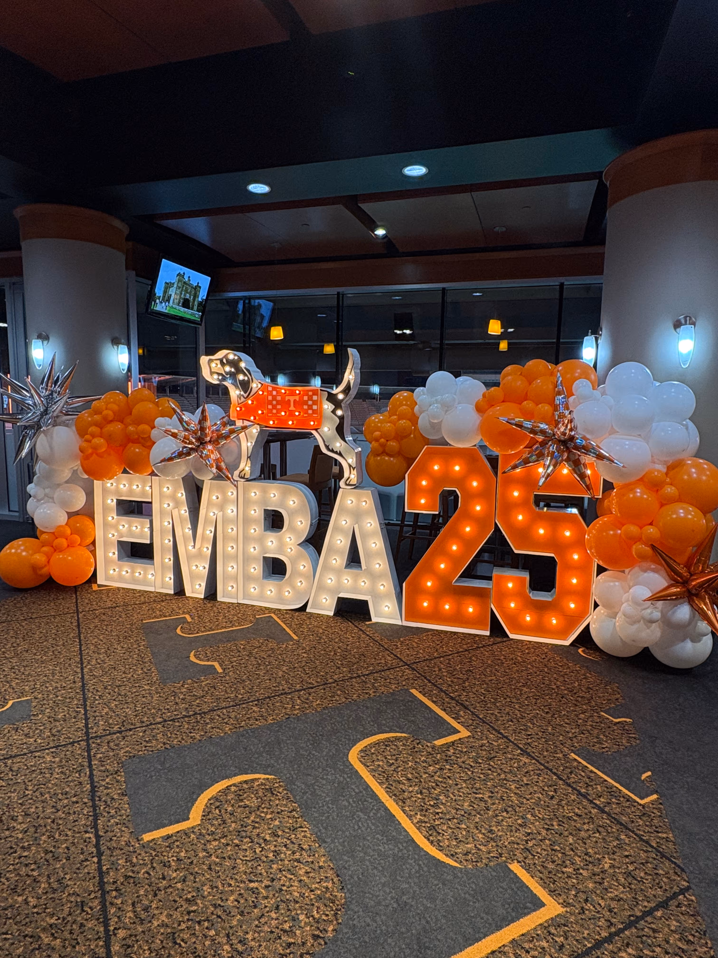 Lit letters spelling HVMS in front of silver and blue balloons at Hardin Valley Middle School with mural stars and music notes on the wall.
