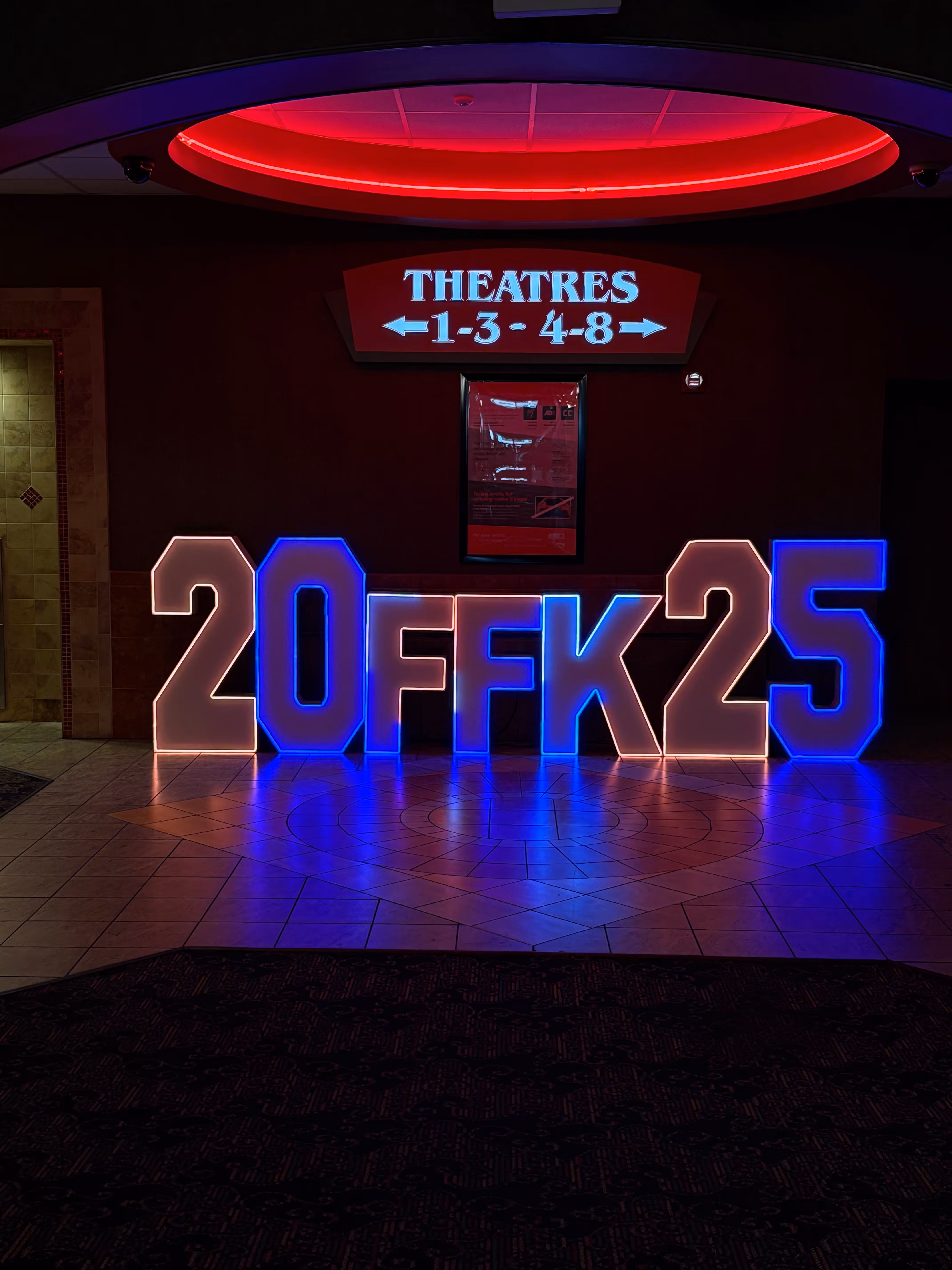 Illuminated sign reading '20FFK25' with a theatre sign above indicating theatres 1-3 to the left and 4-8 to the right.