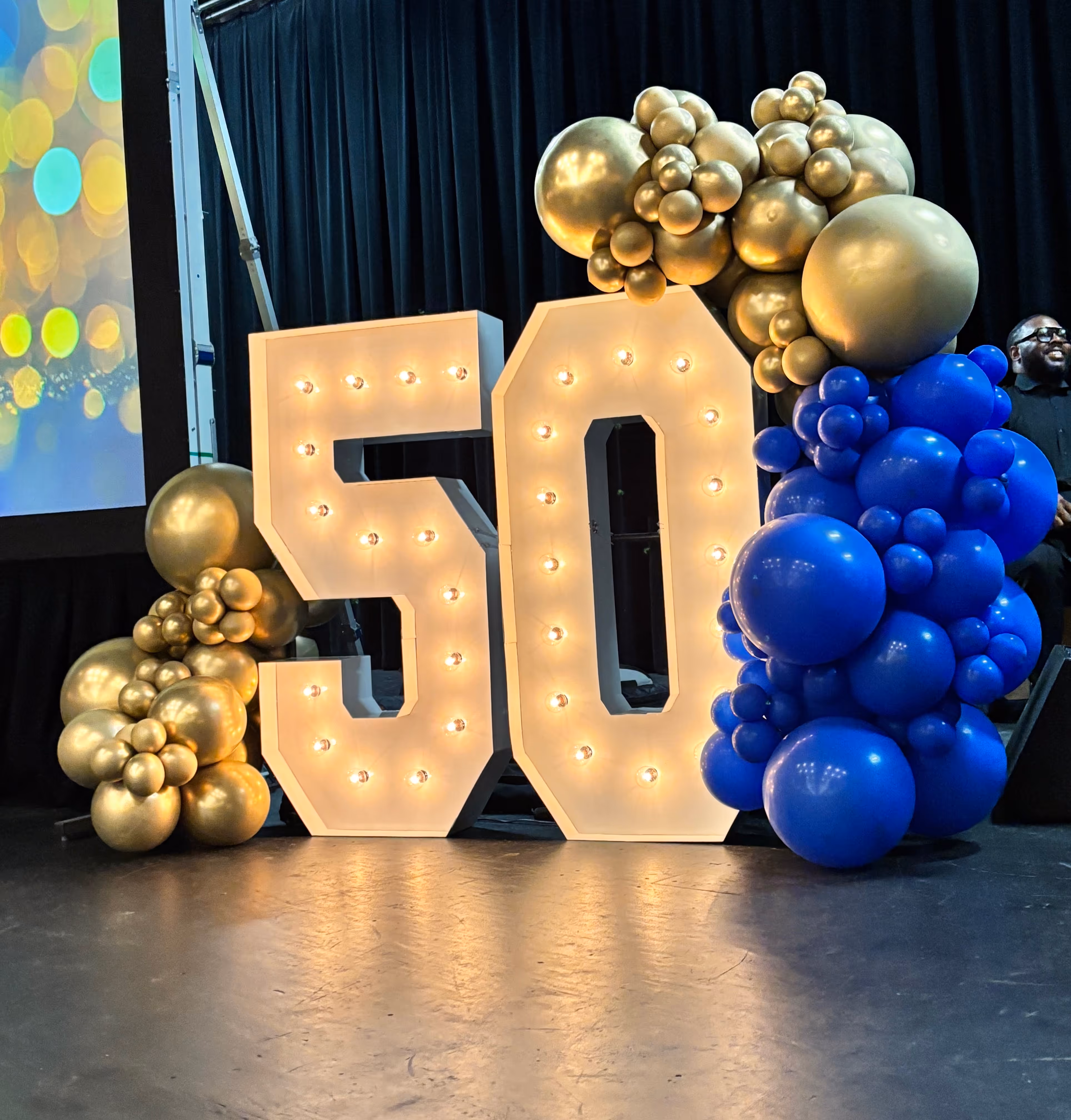 Lit letters spelling HVMS in front of silver and blue balloons at Hardin Valley Middle School with mural stars and music notes on the wall.