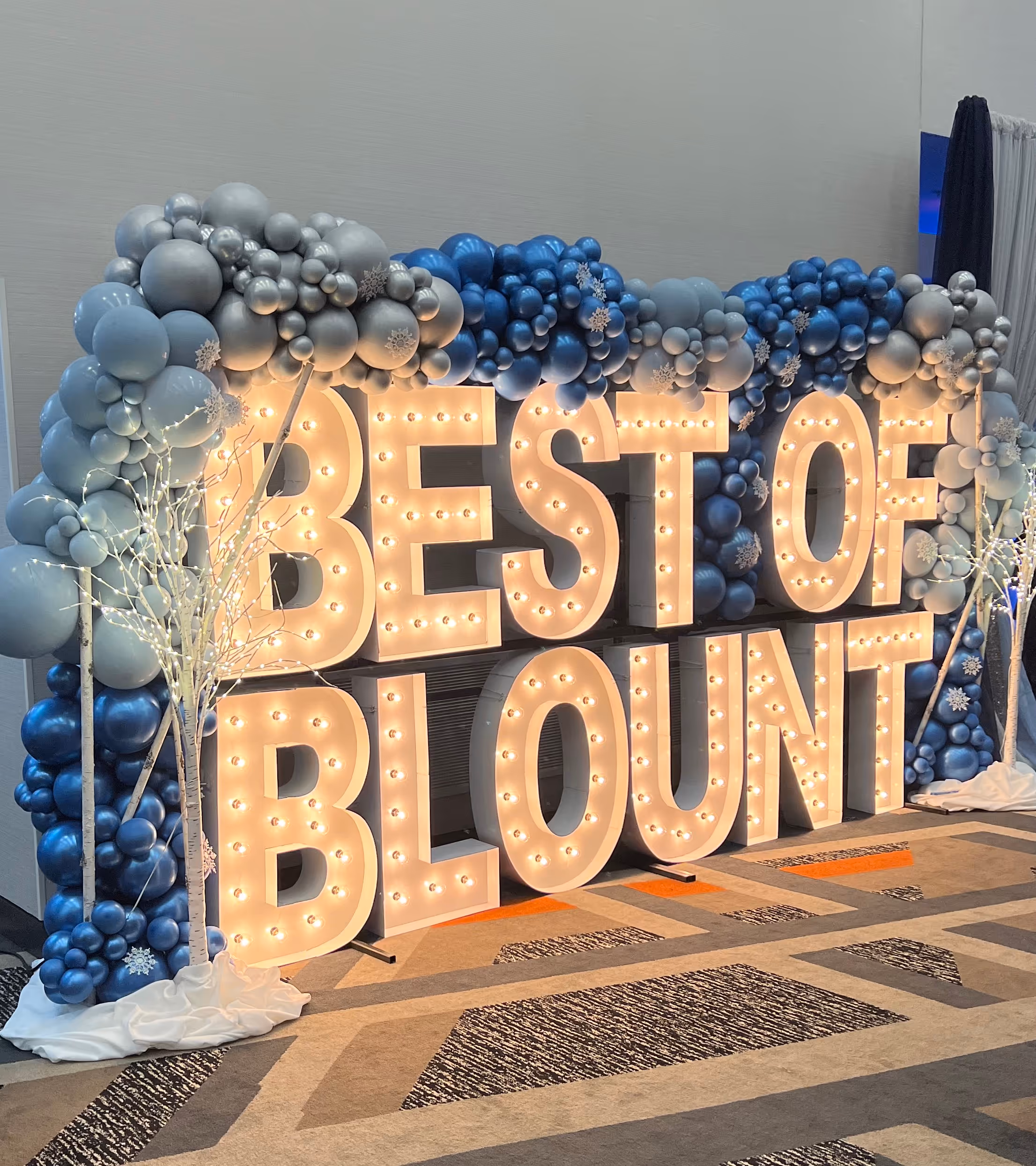 Lit letters spelling HVMS in front of silver and blue balloons at Hardin Valley Middle School with mural stars and music notes on the wall.