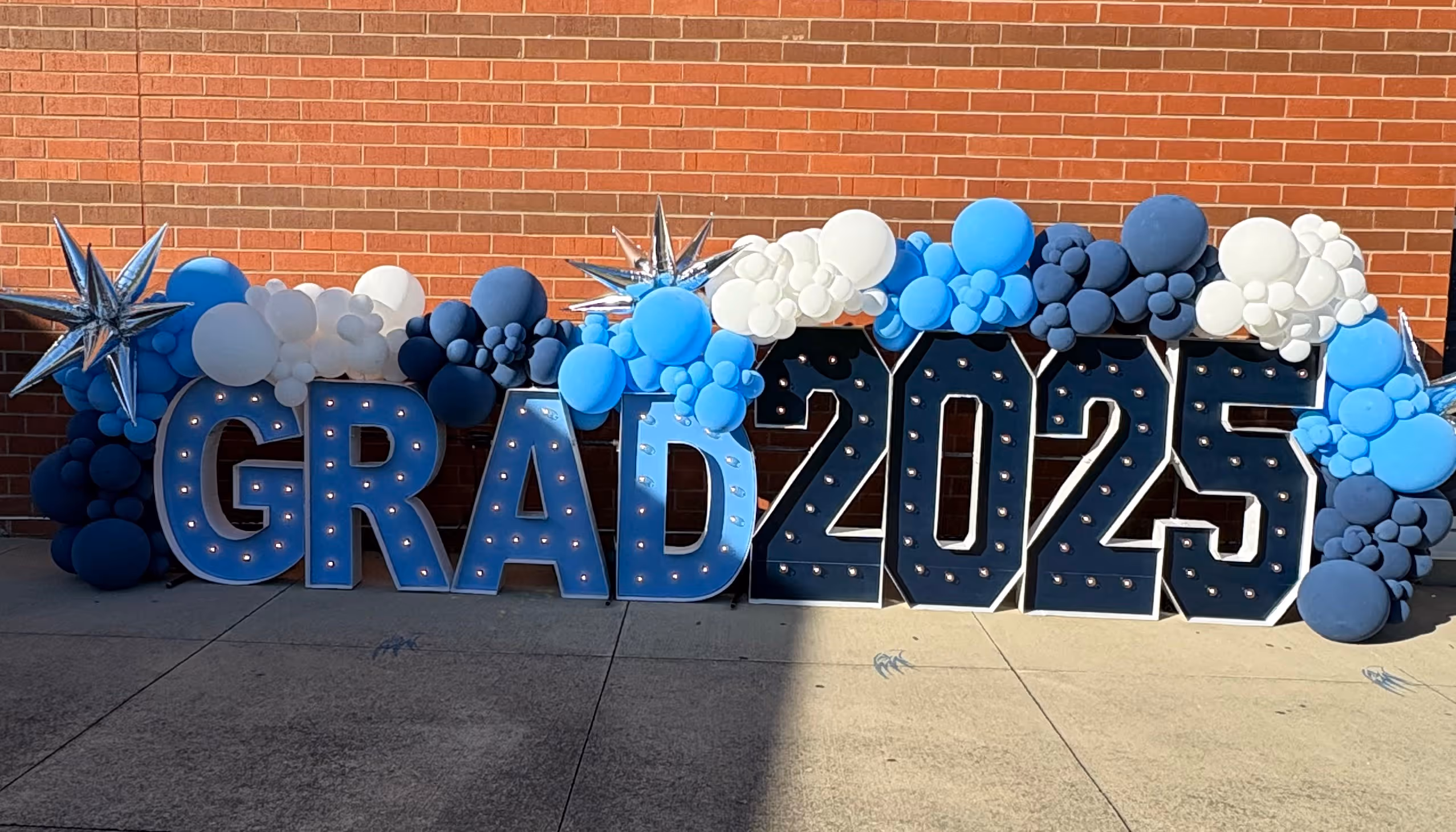 Lit letters spelling HVMS in front of silver and blue balloons at Hardin Valley Middle School with mural stars and music notes on the wall.