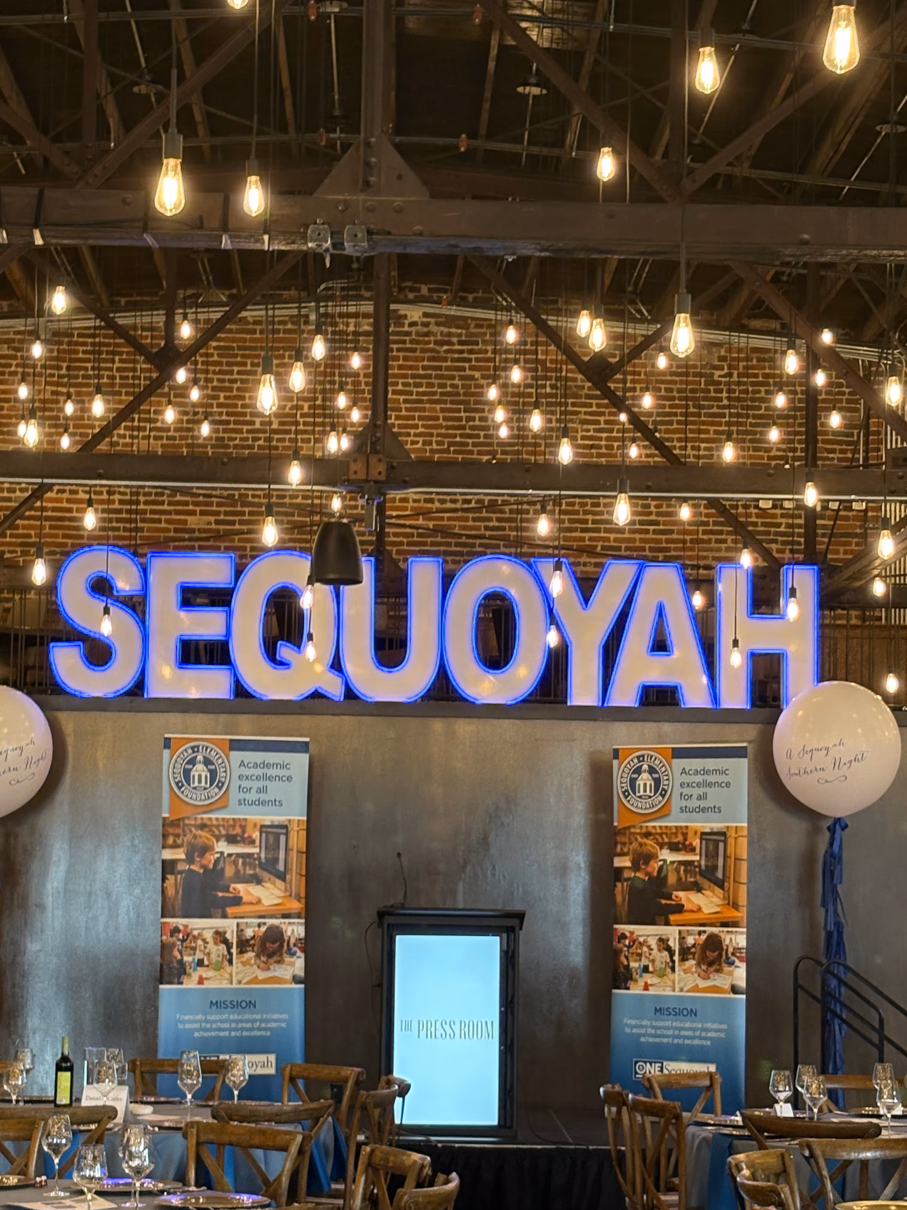 Lit letters spelling HVMS in front of silver and blue balloons at Hardin Valley Middle School with mural stars and music notes on the wall.