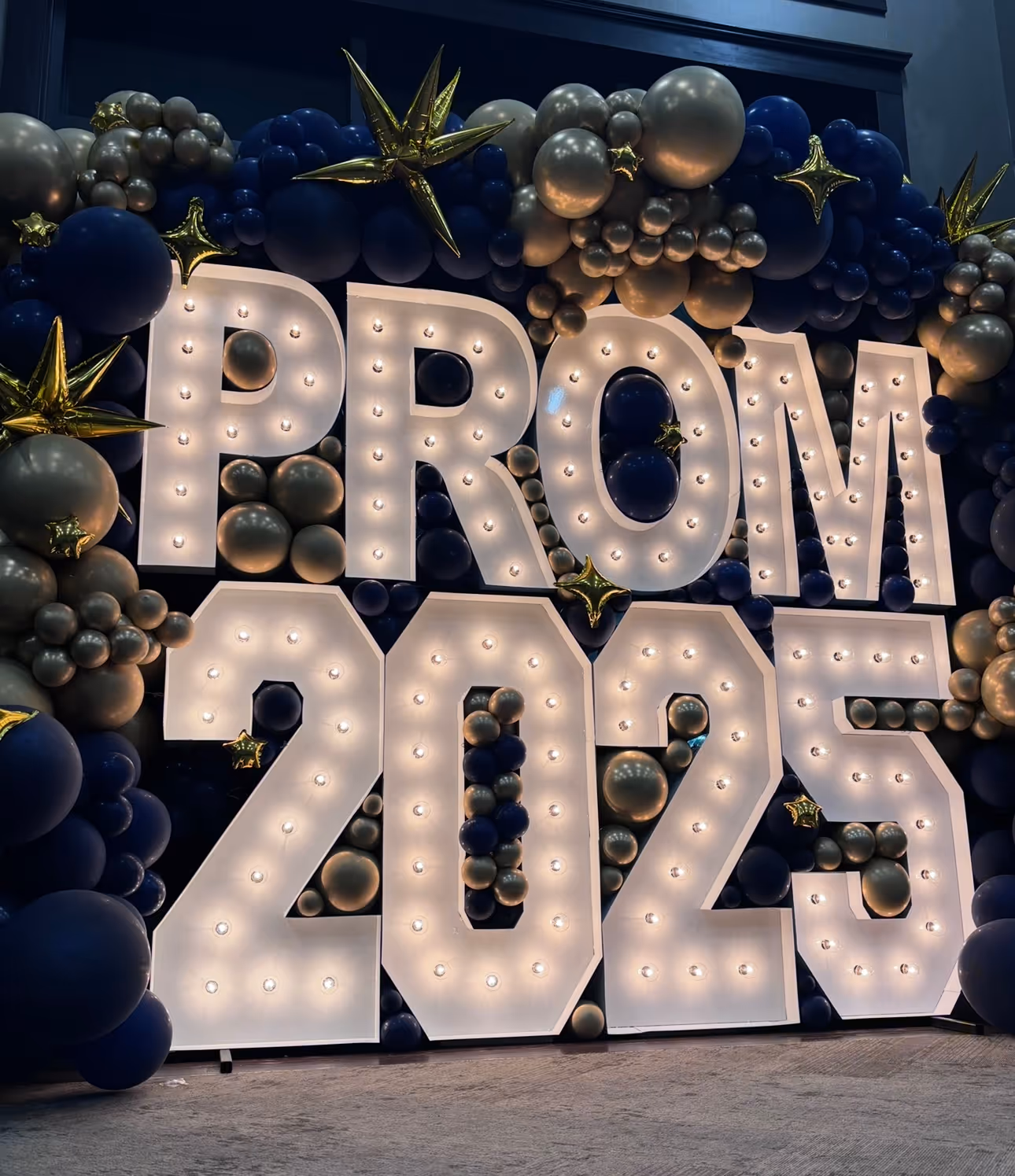 Lit letters spelling HVMS in front of silver and blue balloons at Hardin Valley Middle School with mural stars and music notes on the wall.