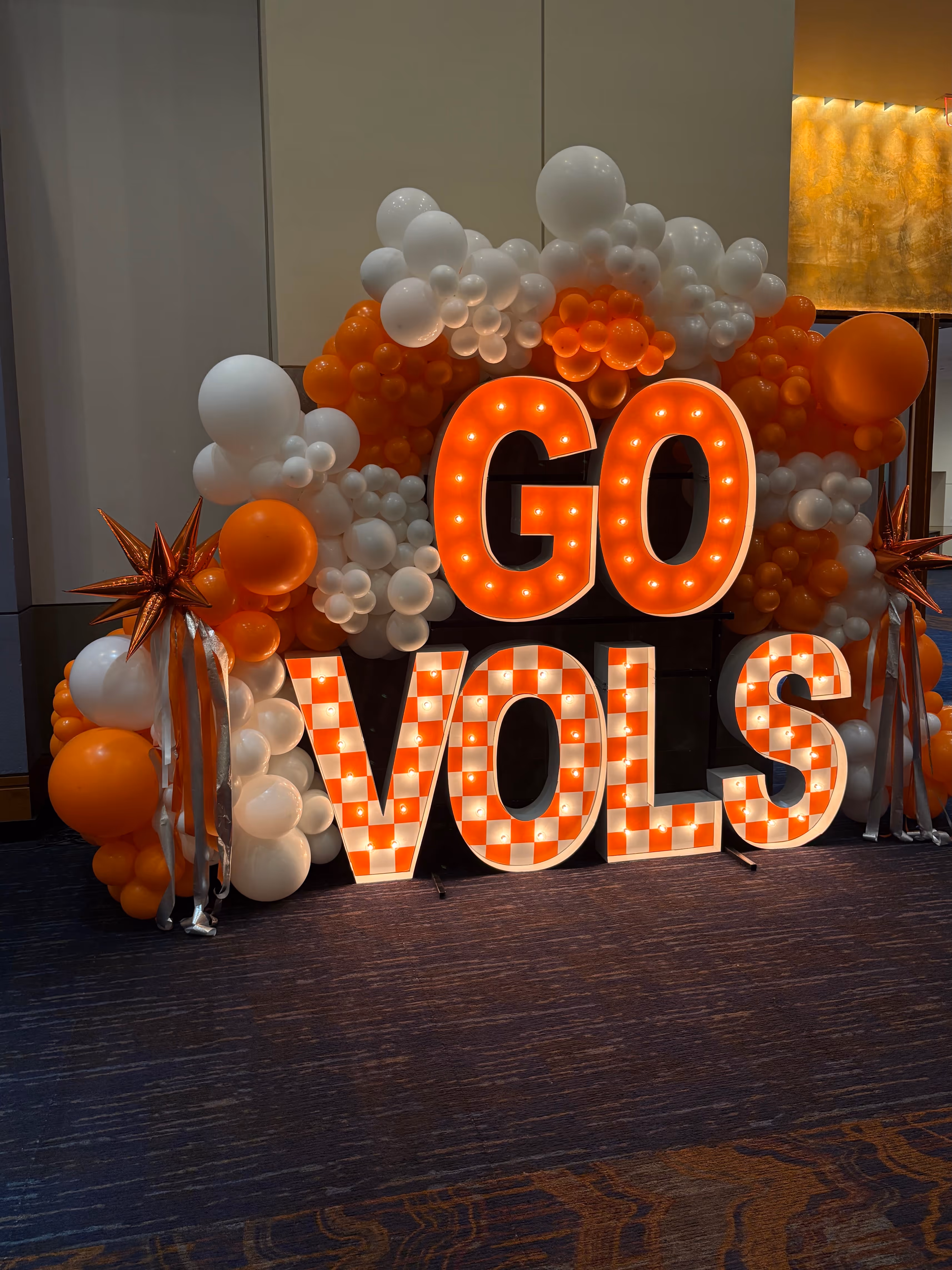 Lit letters spelling HVMS in front of silver and blue balloons at Hardin Valley Middle School with mural stars and music notes on the wall.