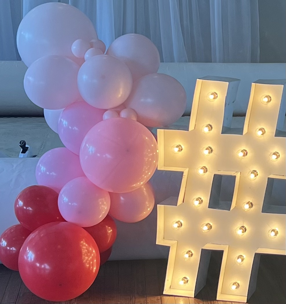 Lit letters spelling HVMS in front of silver and blue balloons at Hardin Valley Middle School with mural stars and music notes on the wall.